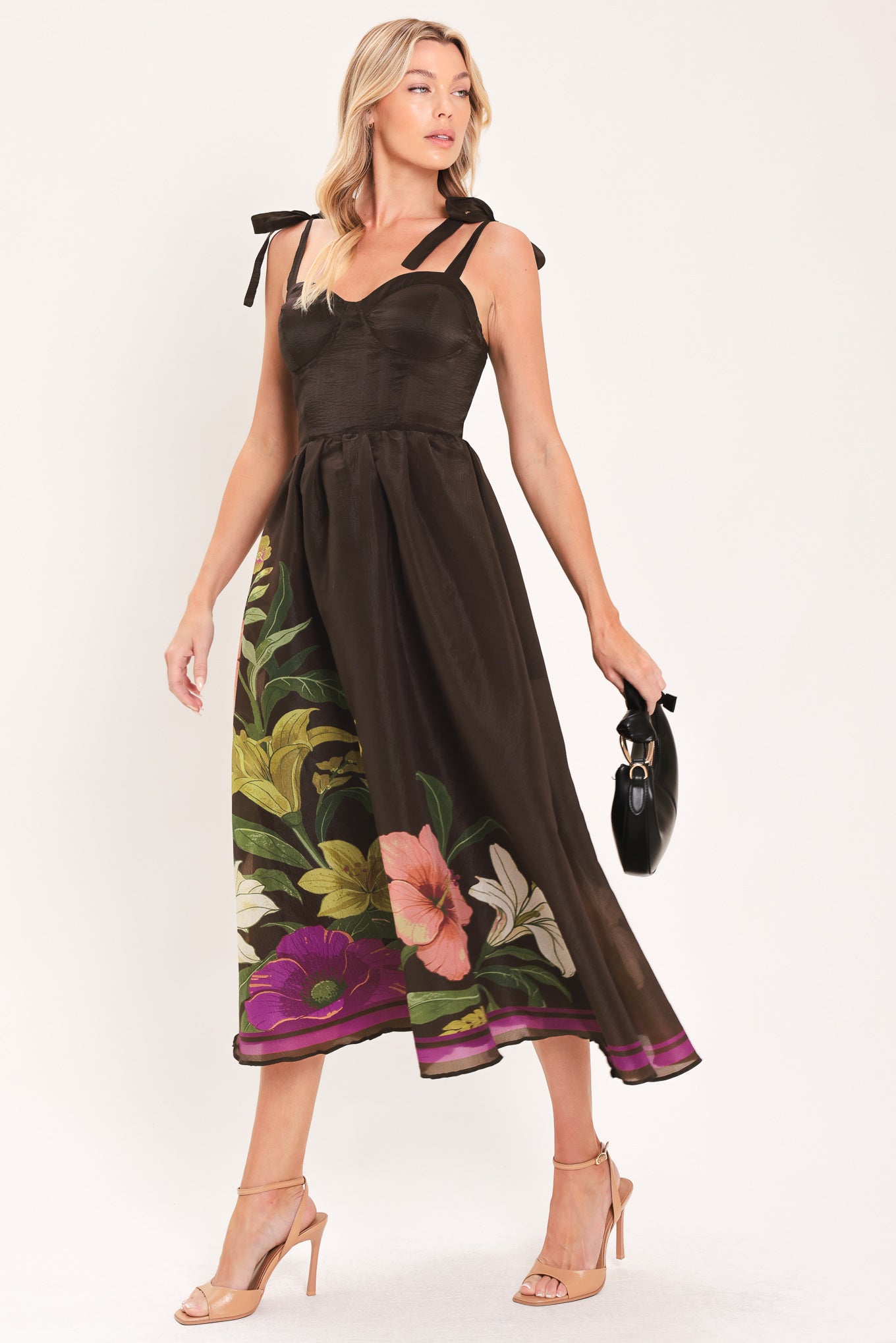 A woman models a sleeveless midi dress with a sweetheart neckline, shoulder straps, and a dark brown base featuring a colorful floral print along the hem and bodice | Flying Tomato
