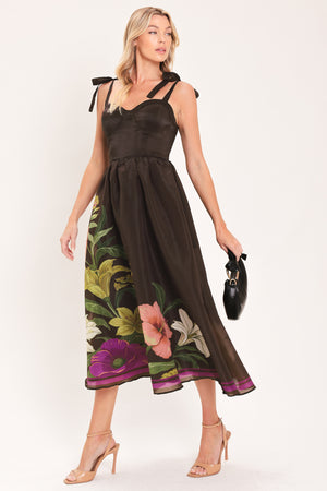 A woman models a sleeveless midi dress with a sweetheart neckline, shoulder straps, and a dark brown base featuring a colorful floral print along the hem and bodice | Flying Tomato