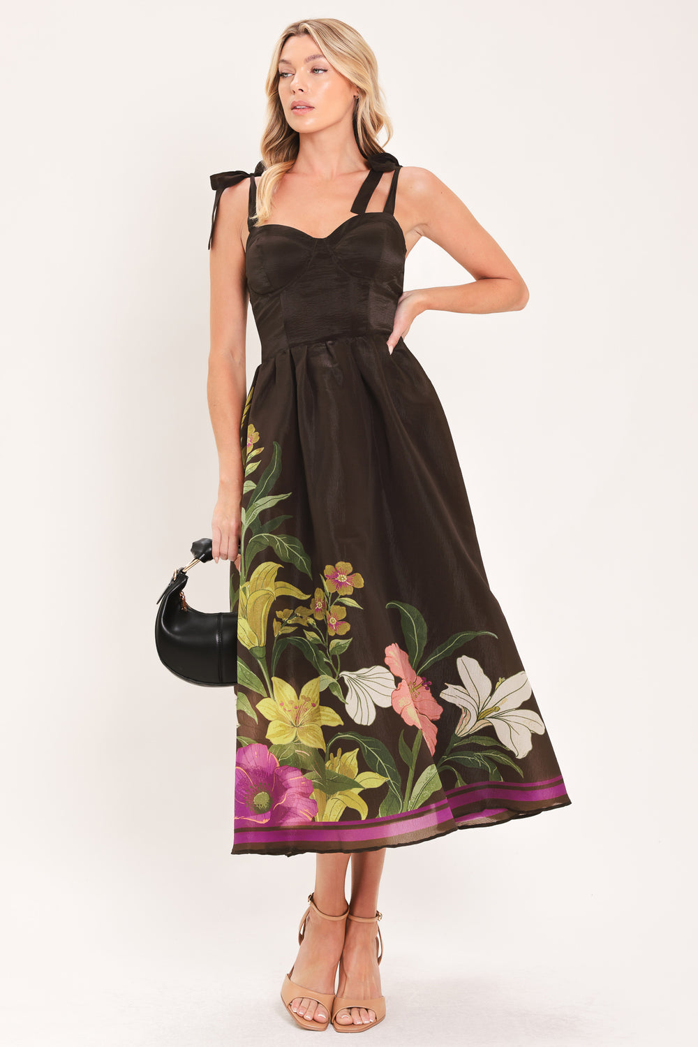 A woman models a sleeveless midi dress with a sweetheart neckline, shoulder straps, and a dark brown base featuring a colorful floral print along the hem and bodice | Flying Tomato