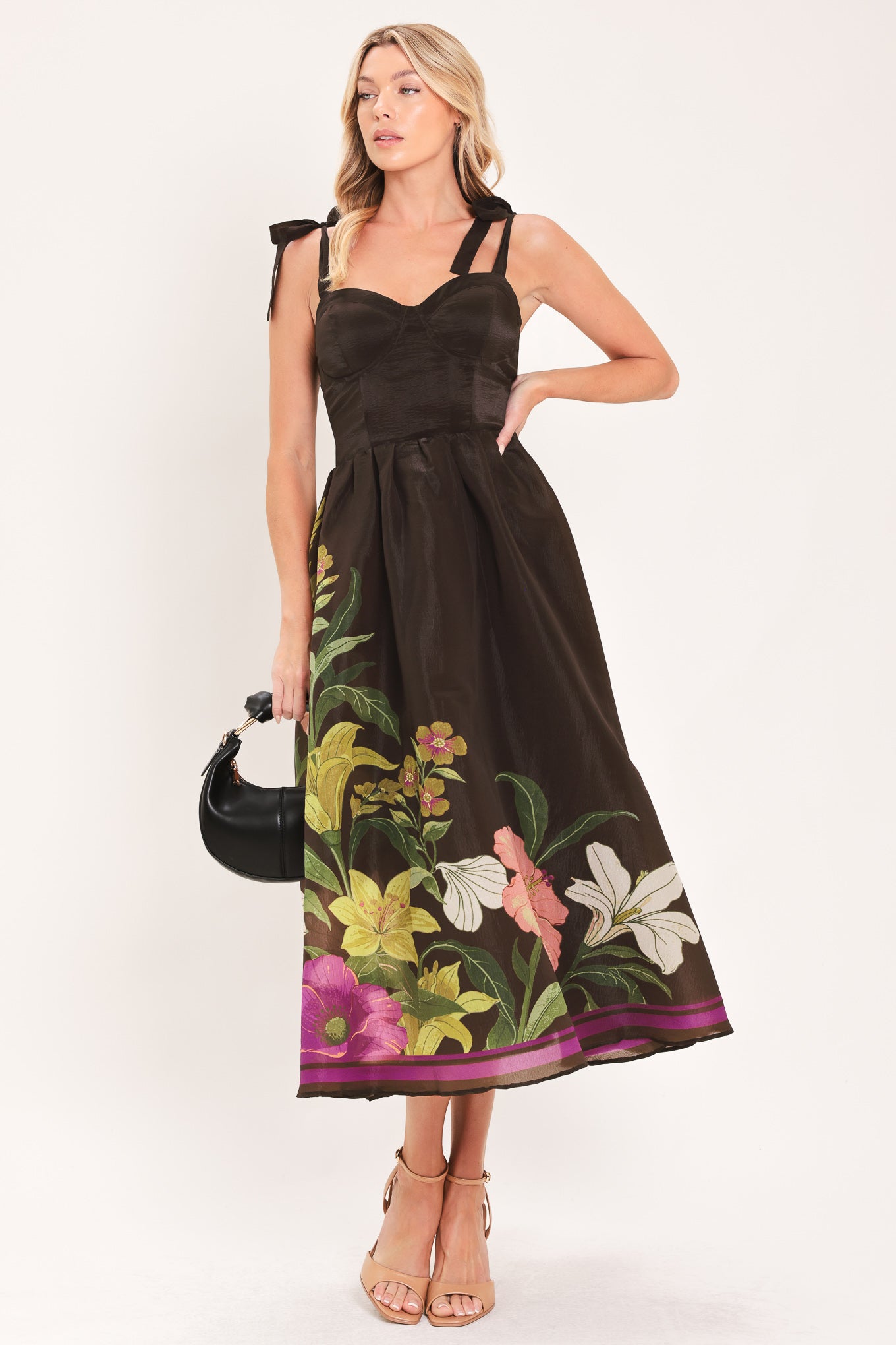 A woman models a sleeveless midi dress with a sweetheart neckline, shoulder straps, and a dark brown base featuring a colorful floral print along the hem and bodice | Flying Tomato