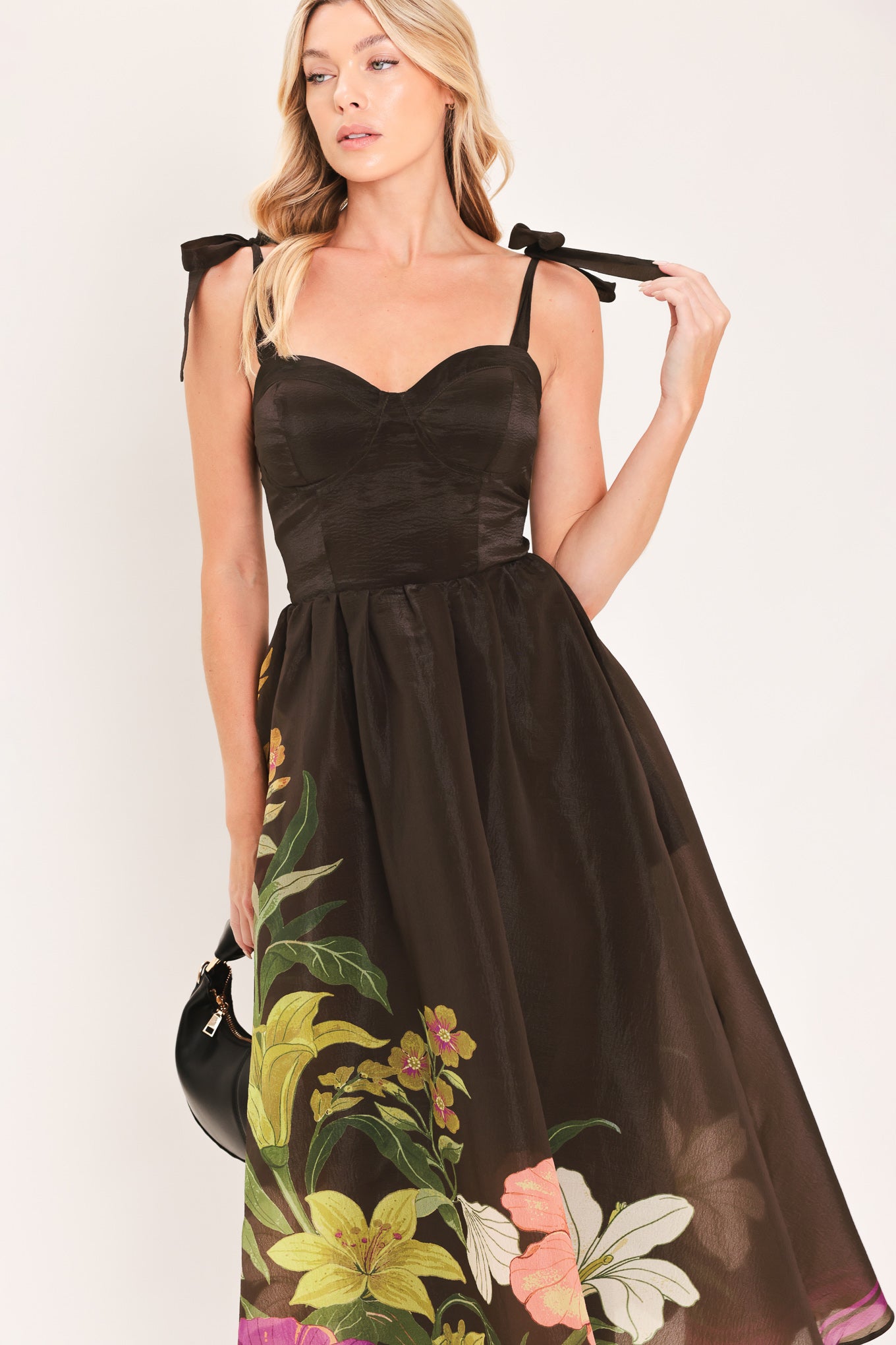 A woman models a sleeveless midi dress with a sweetheart neckline, shoulder straps, and a dark brown base featuring a colorful floral print along the hem and bodice | Flying Tomato
