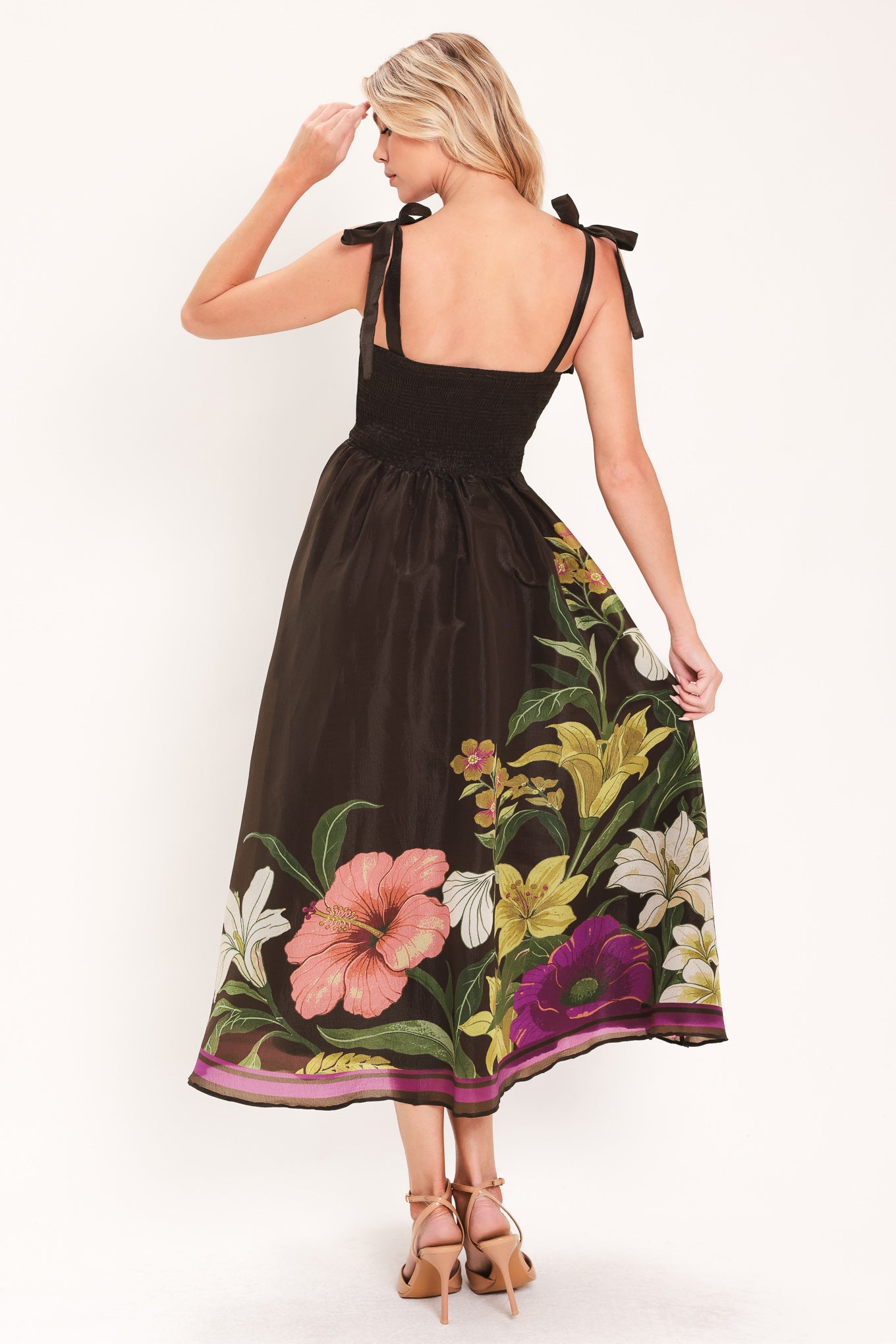 A woman models a sleeveless midi dress with a sweetheart neckline, shoulder straps, and a dark brown base featuring a colorful floral print along the hem and bodice | Flying Tomato
