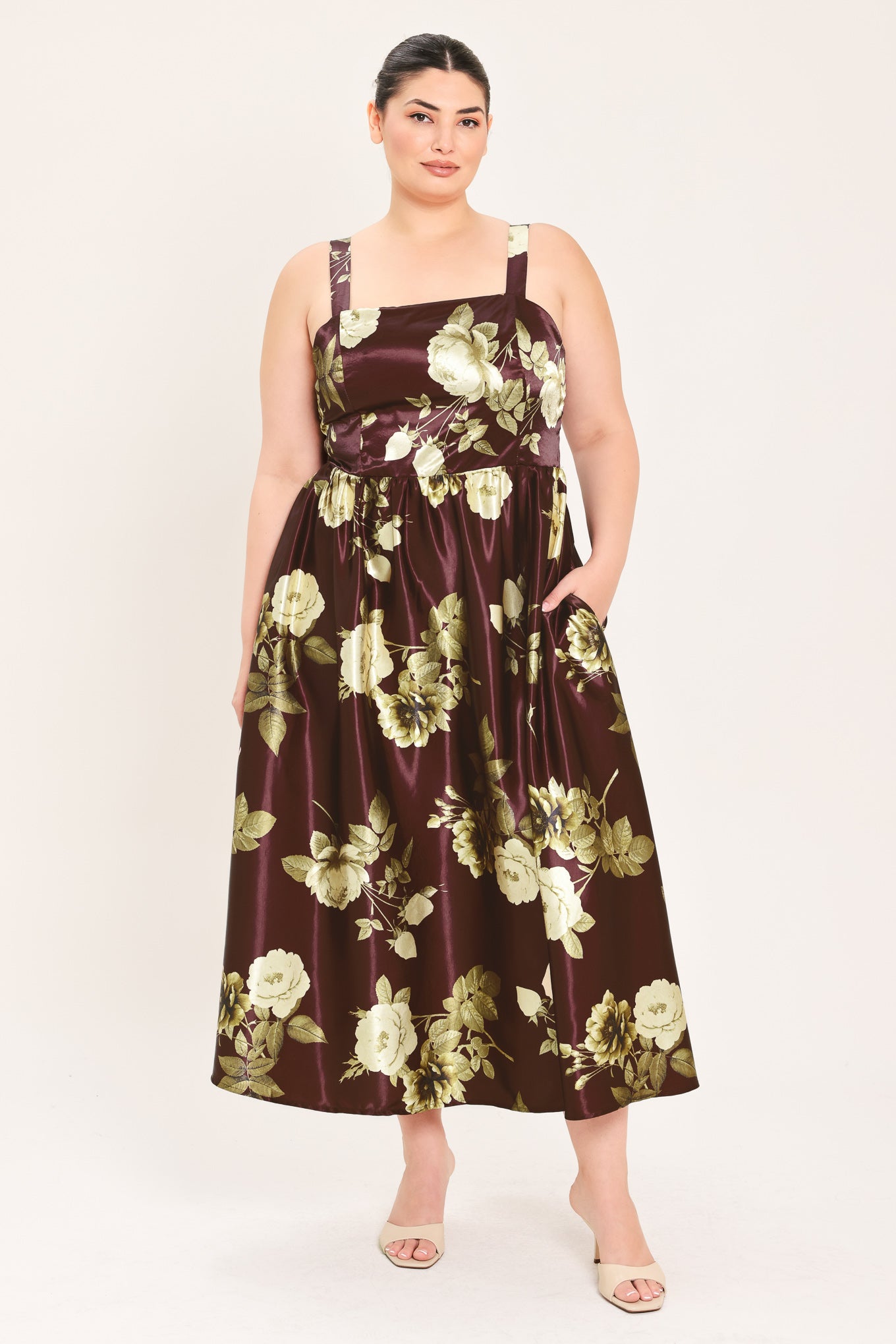 A woman modeling a sleeveless midi dress with a brown satin-like base and a large cream and olive floral print | Flying Tomato Curve