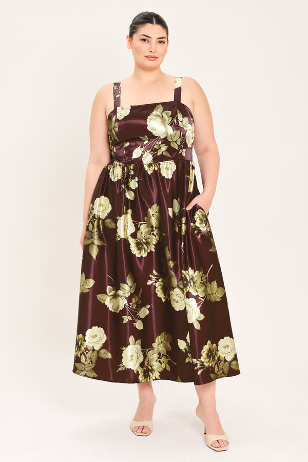 A woman modeling a sleeveless midi dress with a brown satin-like base and a large cream and olive floral print | Flying Tomato Curve