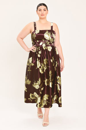A woman modeling a sleeveless midi dress with a brown satin-like base and a large cream and olive floral print | Flying Tomato Curve