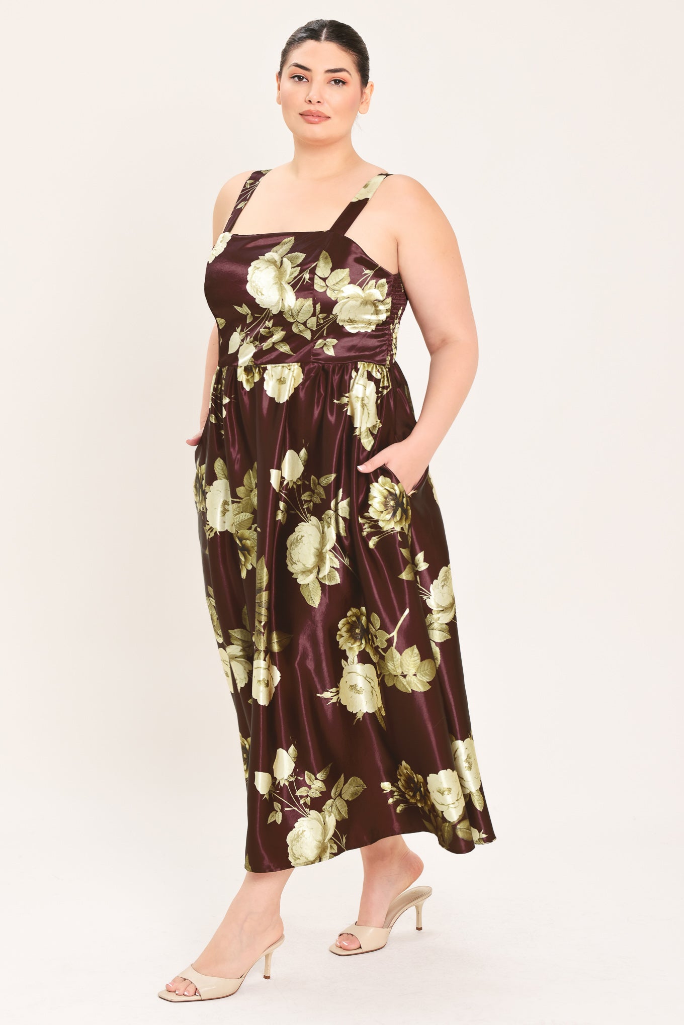 A woman modeling a sleeveless midi dress with a brown satin-like base and a large cream and olive floral print | Flying Tomato Curve