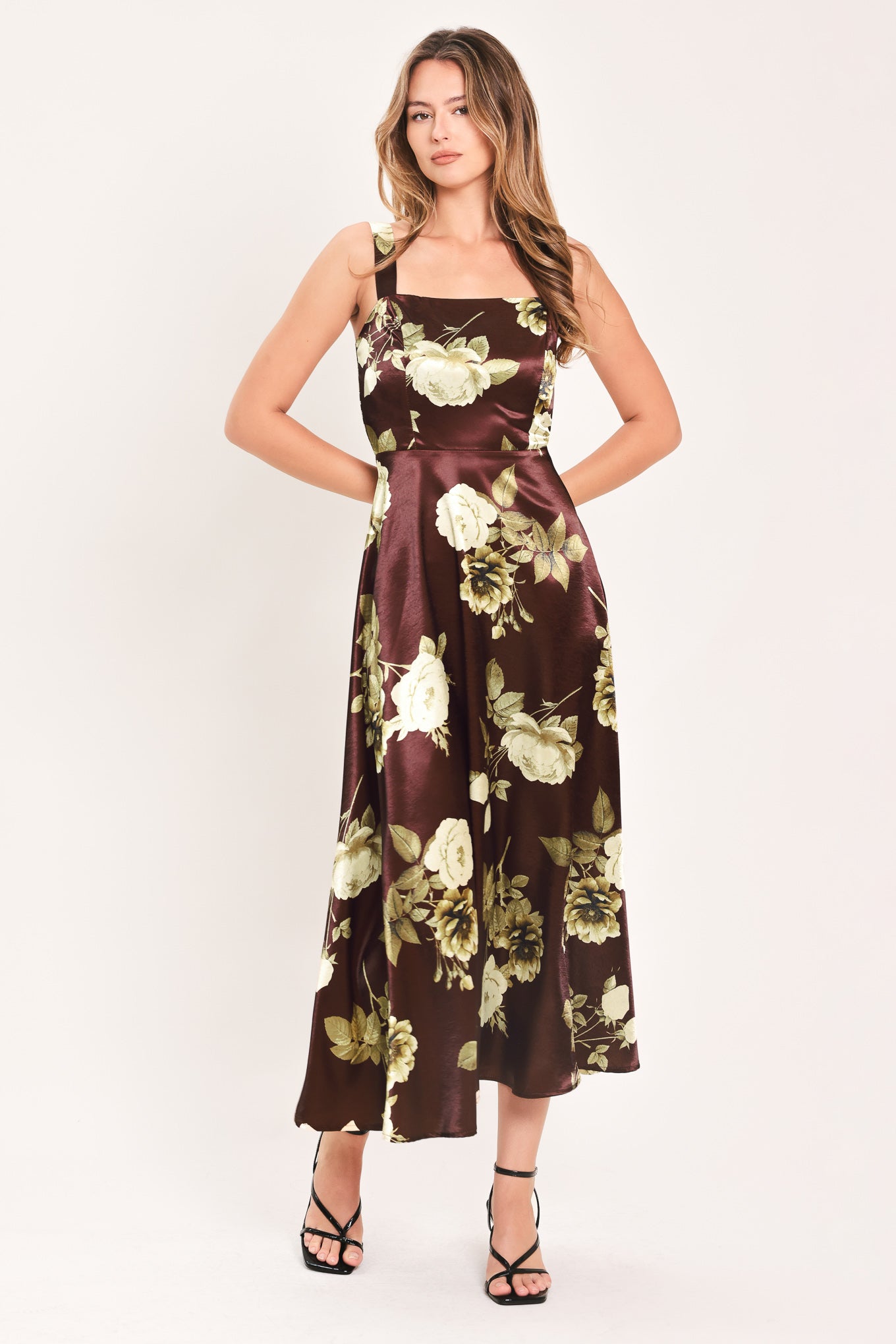 A woman modeling a sleeveless midi dress with a brown satin-like base and a large cream and olive floral print | Flying Tomato