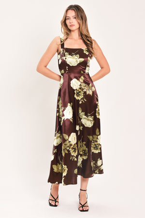 A woman modeling a sleeveless midi dress with a brown satin-like base and a large cream and olive floral print | Flying Tomato