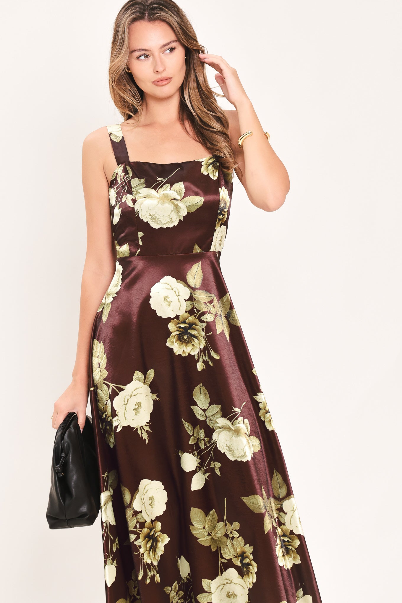 A woman modeling a sleeveless midi dress with a brown satin-like base and a large cream and olive floral print | Flying Tomato