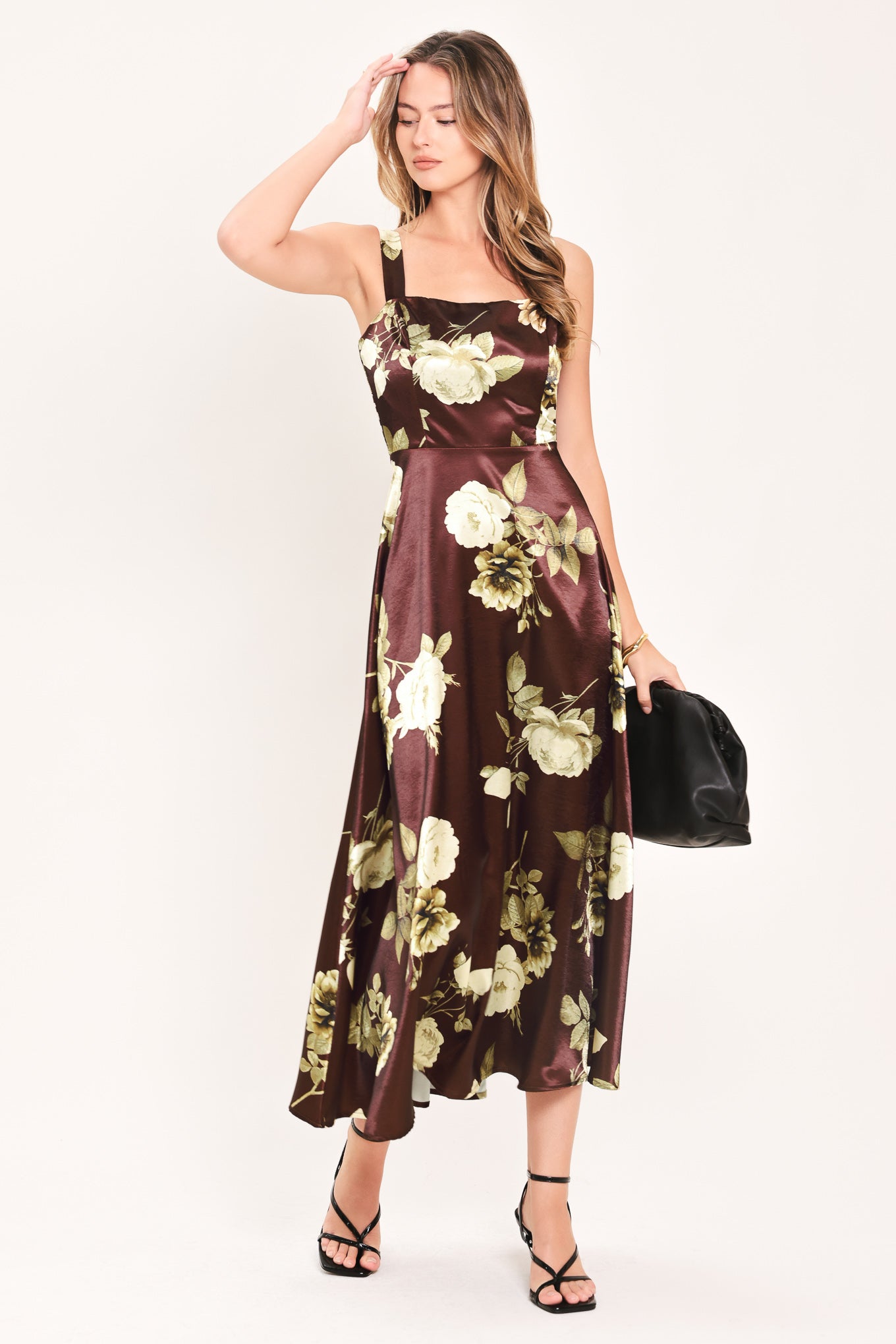 A woman modeling a sleeveless midi dress with a brown satin-like base and a large cream and olive floral print | Flying Tomato