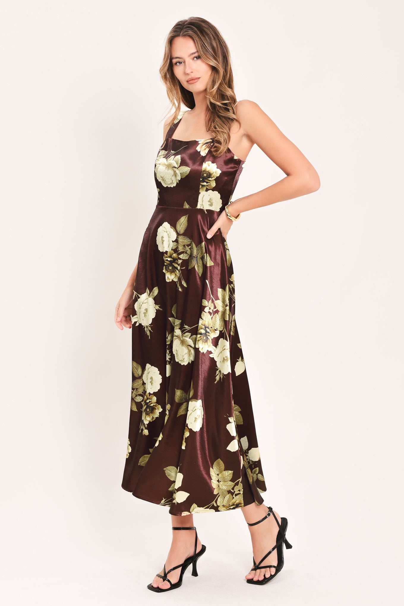 A woman modeling a sleeveless midi dress with a brown satin-like base and a large cream and olive floral print | Flying Tomato