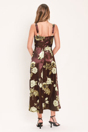 A woman modeling a sleeveless midi dress with a brown satin-like base and a large cream and olive floral print | Flying Tomato