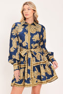 A woman modeling a long-sleeve mini dress with a blue and gold paisley pattern, featuring a button-up front, tie waist, and flared skirt | Flying Tomato