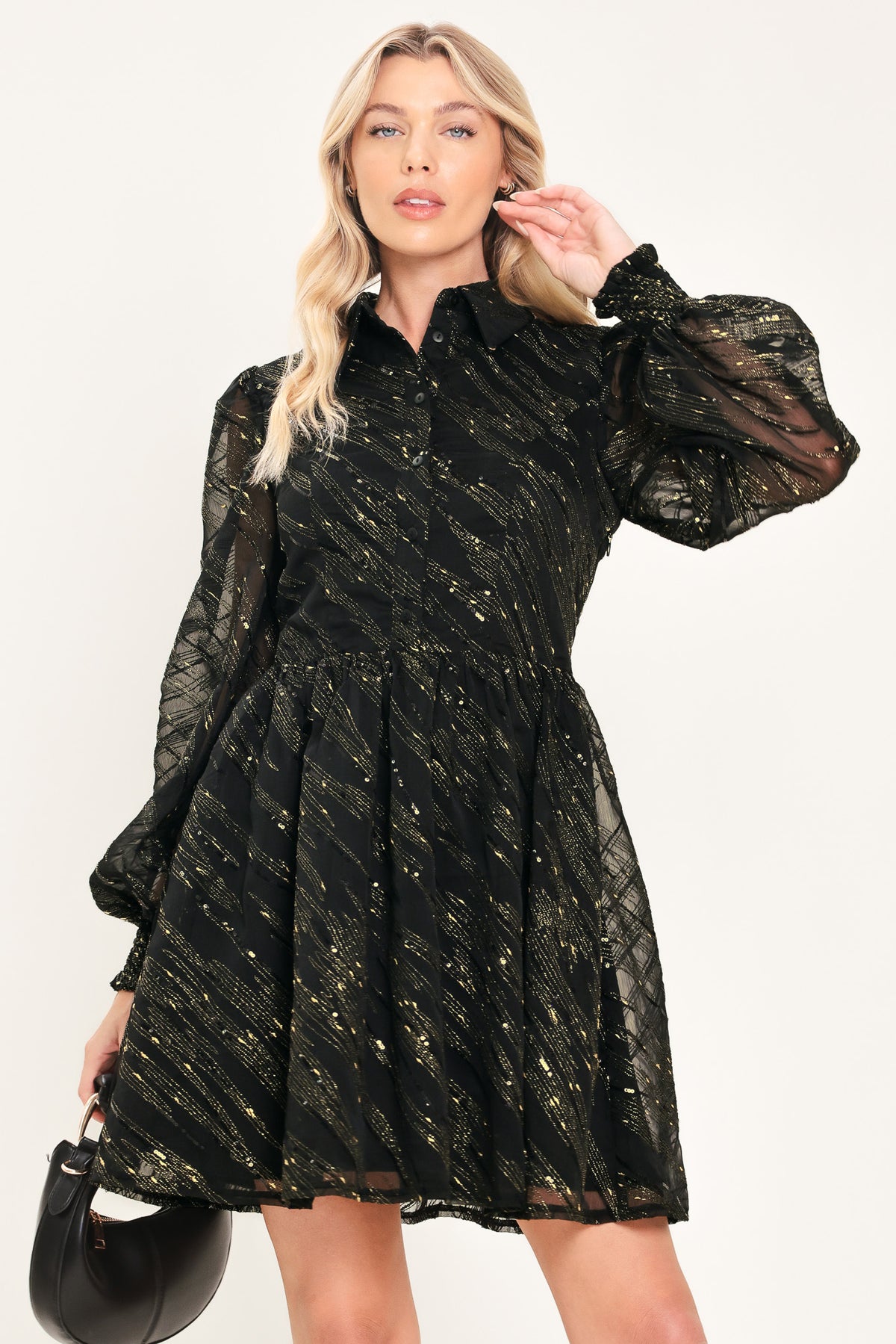 A model wearing a black sheer mini dress with gold glittery diagonal stripes, featuring long balloon sleeves and a flared skirt | Flying Tomato