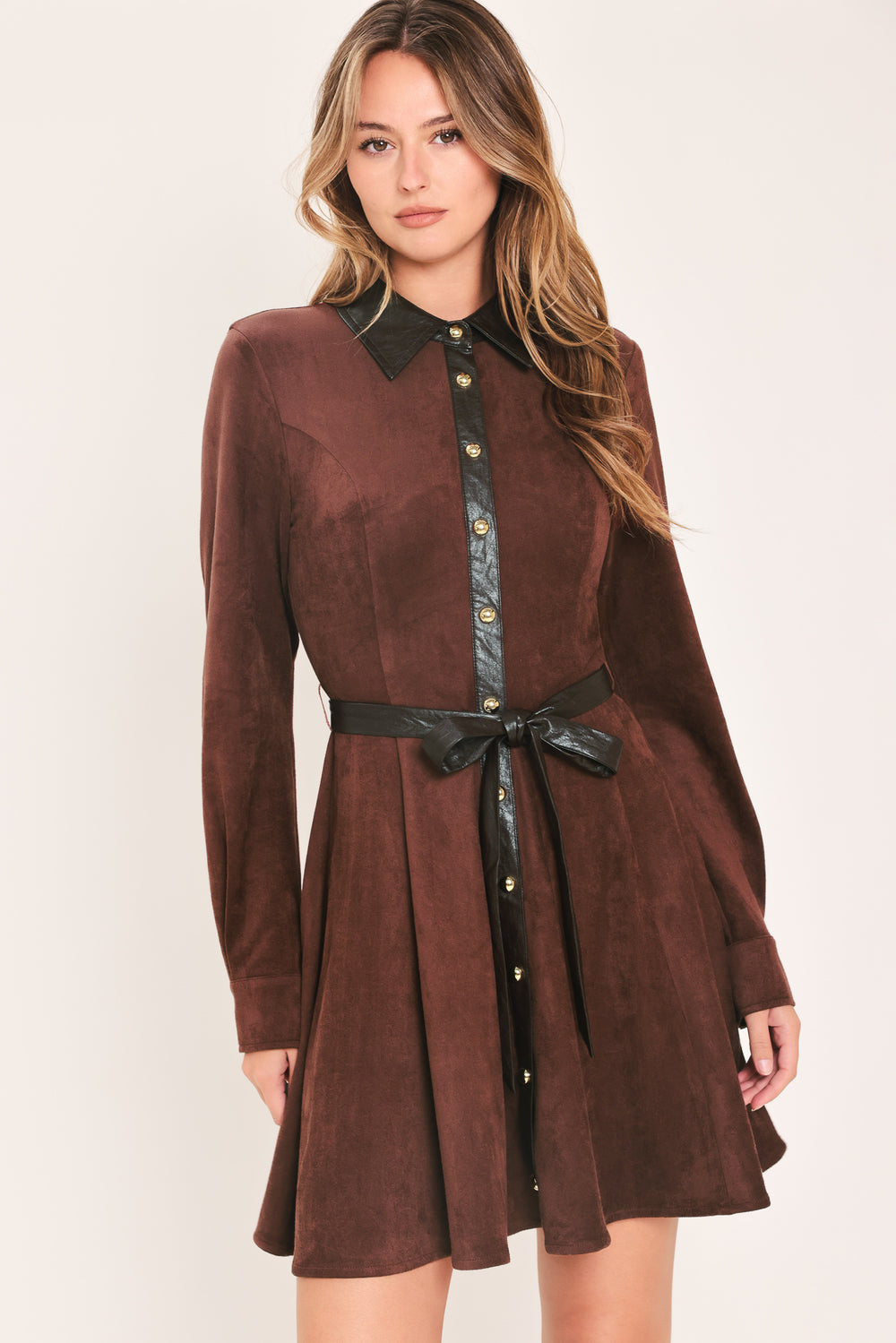 A woman modeling a brown suede long-sleeve shirt dress with a black faux-leather collar, button placket, and matching black tie belt | Flying Tomato
