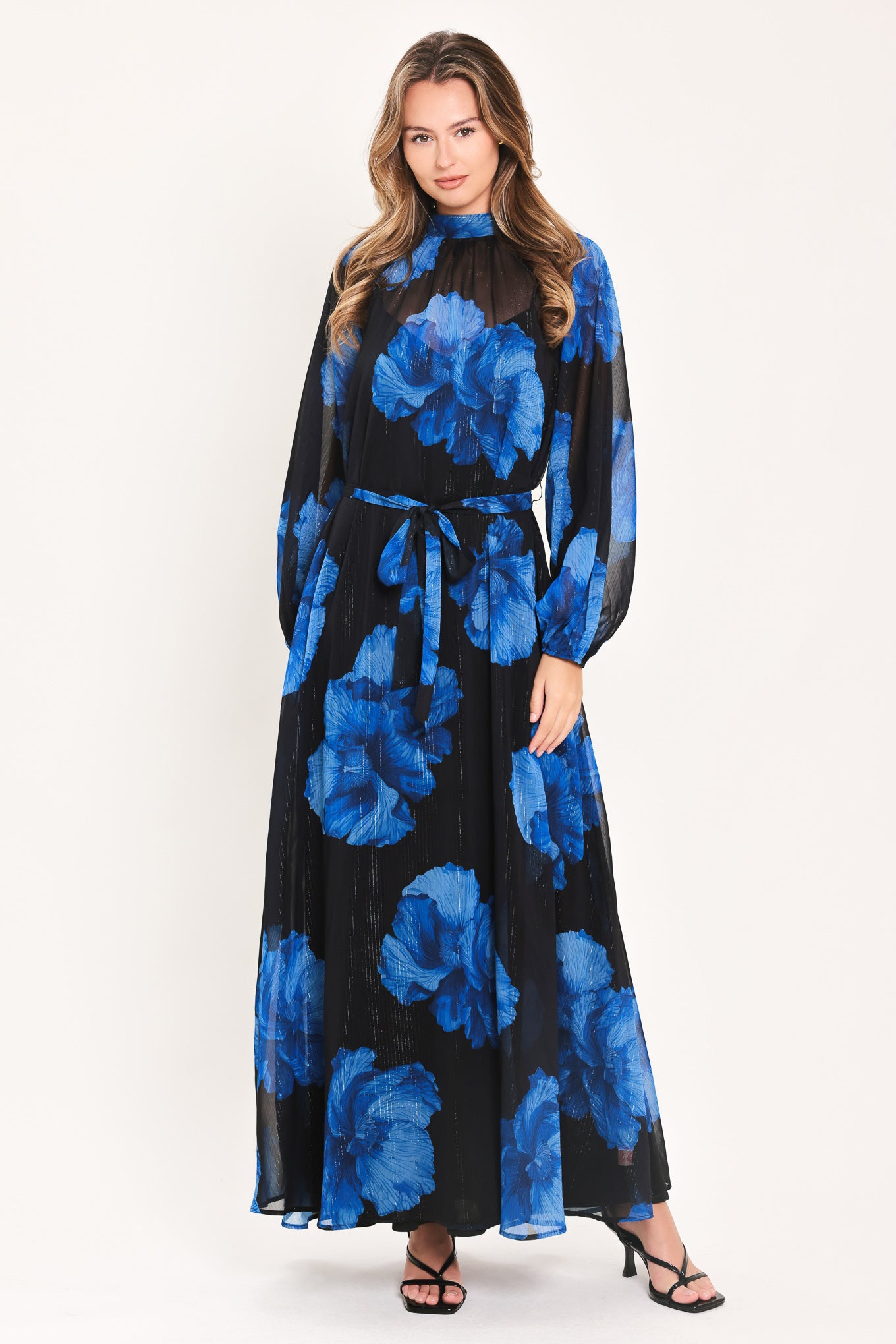 A woman modeling a long-sleeve maxi dress with a black base and a vibrant blue floral print | Flying Tomato