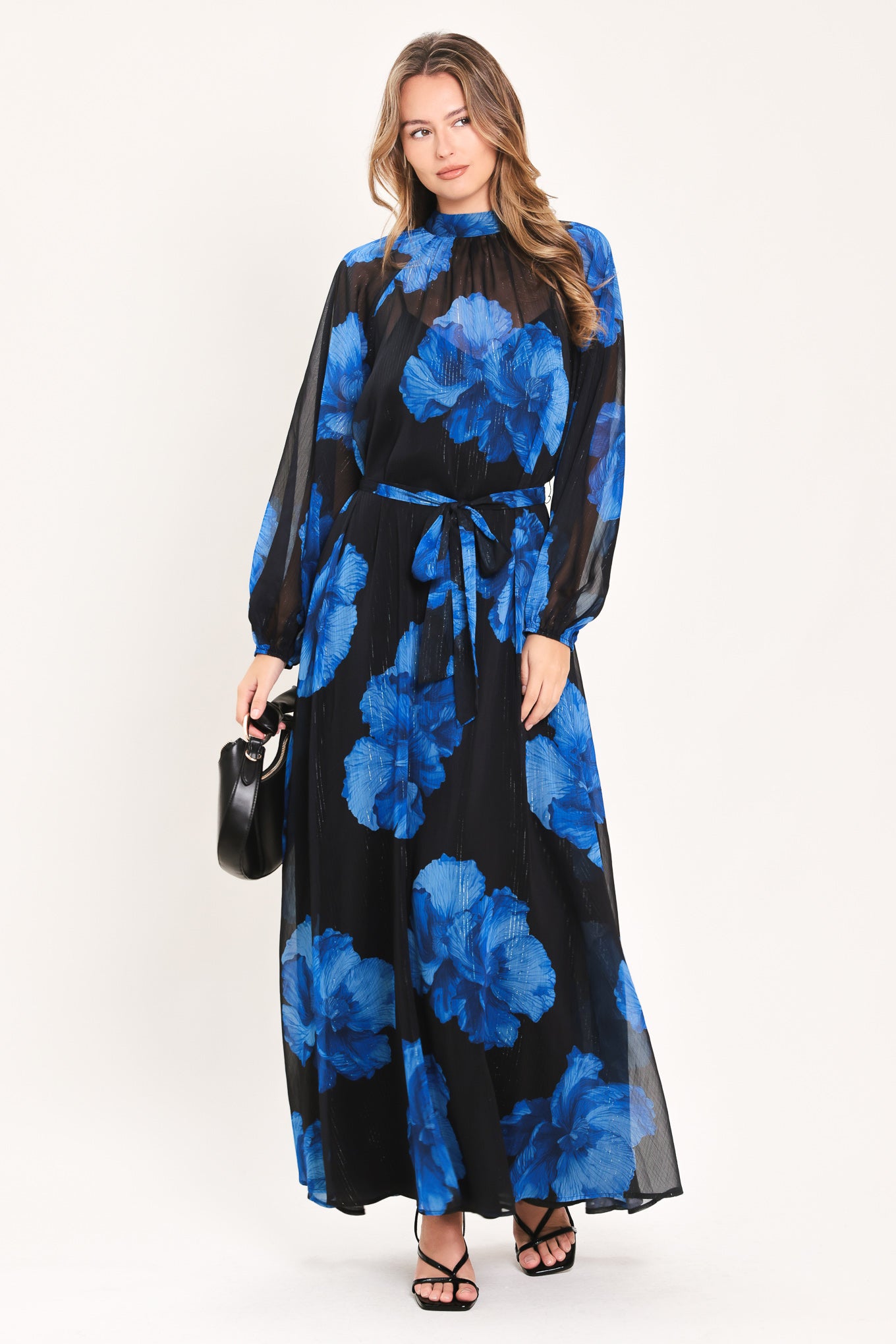 A woman modeling a long-sleeve maxi dress with a black base and a vibrant blue floral print | Flying Tomato