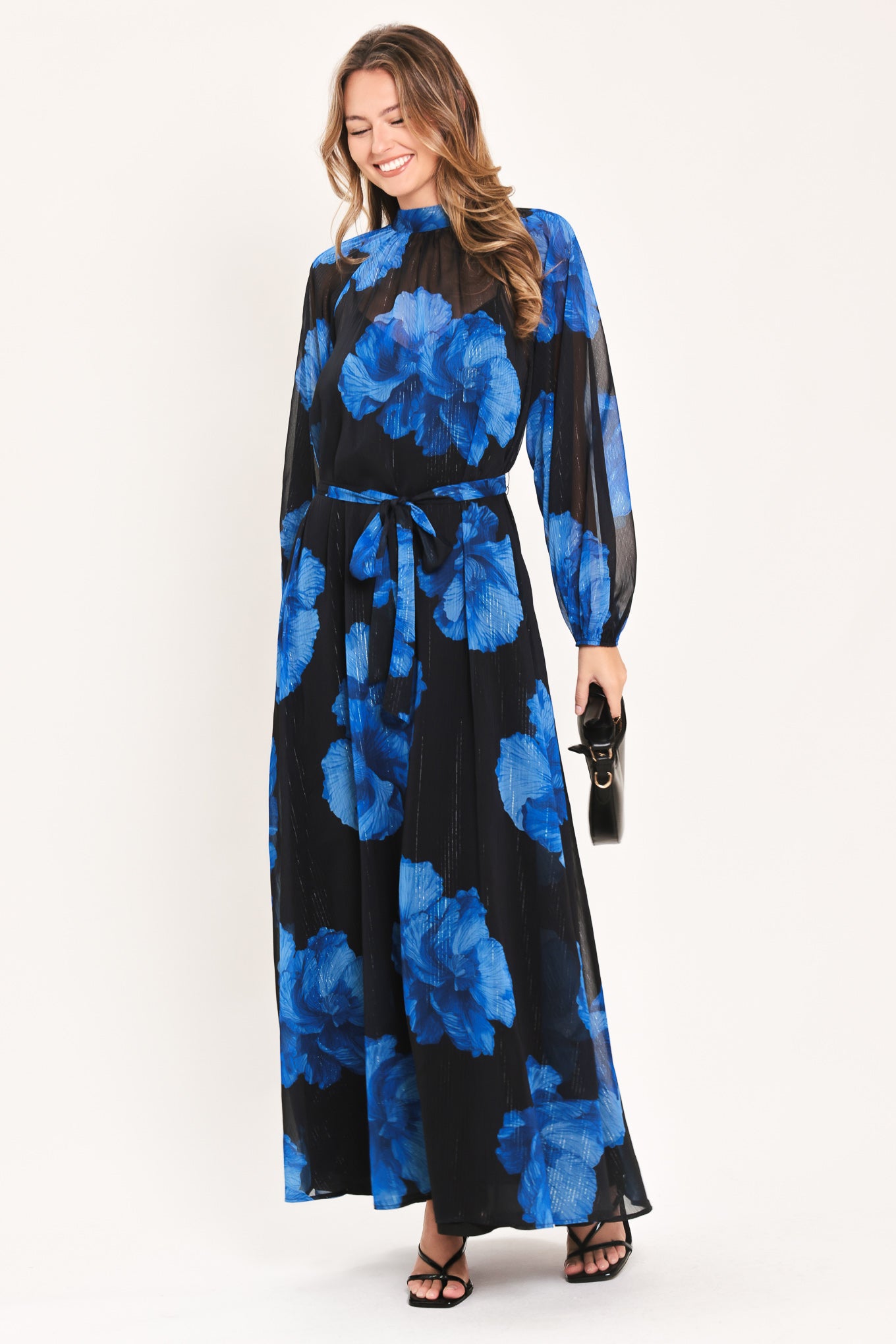 A woman modeling a long-sleeve maxi dress with a black base and a vibrant blue floral print | Flying Tomato