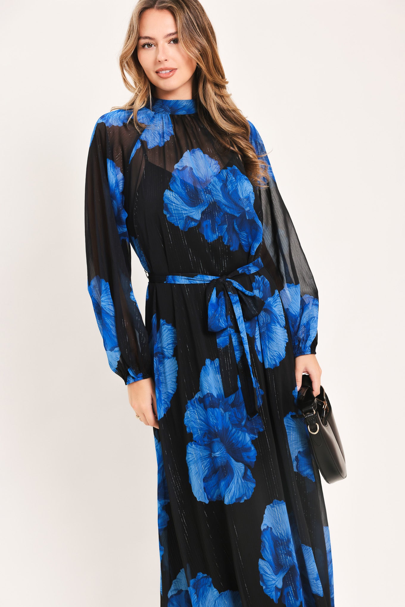 A woman modeling a long-sleeve maxi dress with a black base and a vibrant blue floral print | Flying Tomato