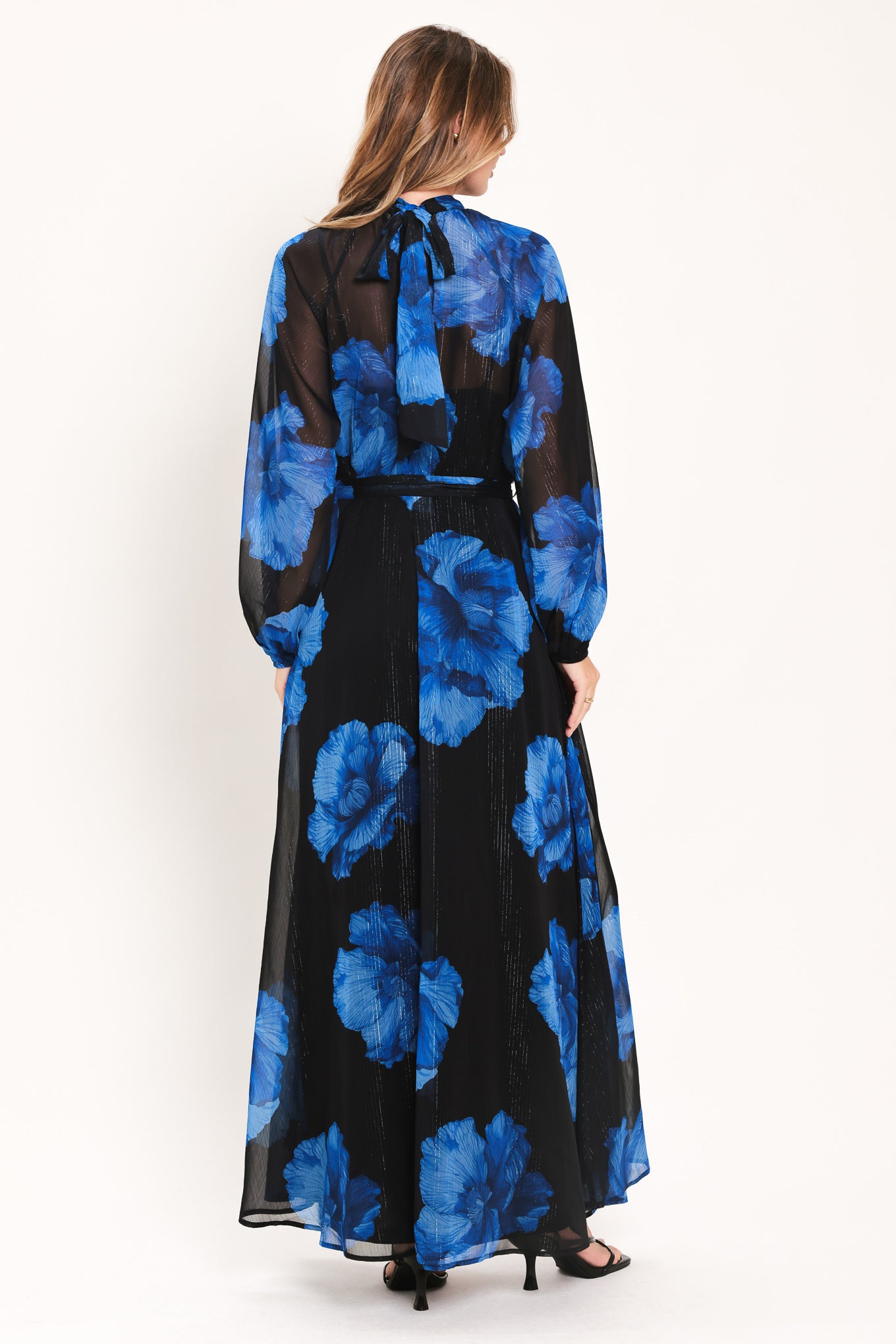 A woman modeling a long-sleeve maxi dress with a black base and a vibrant blue floral print | Flying Tomato