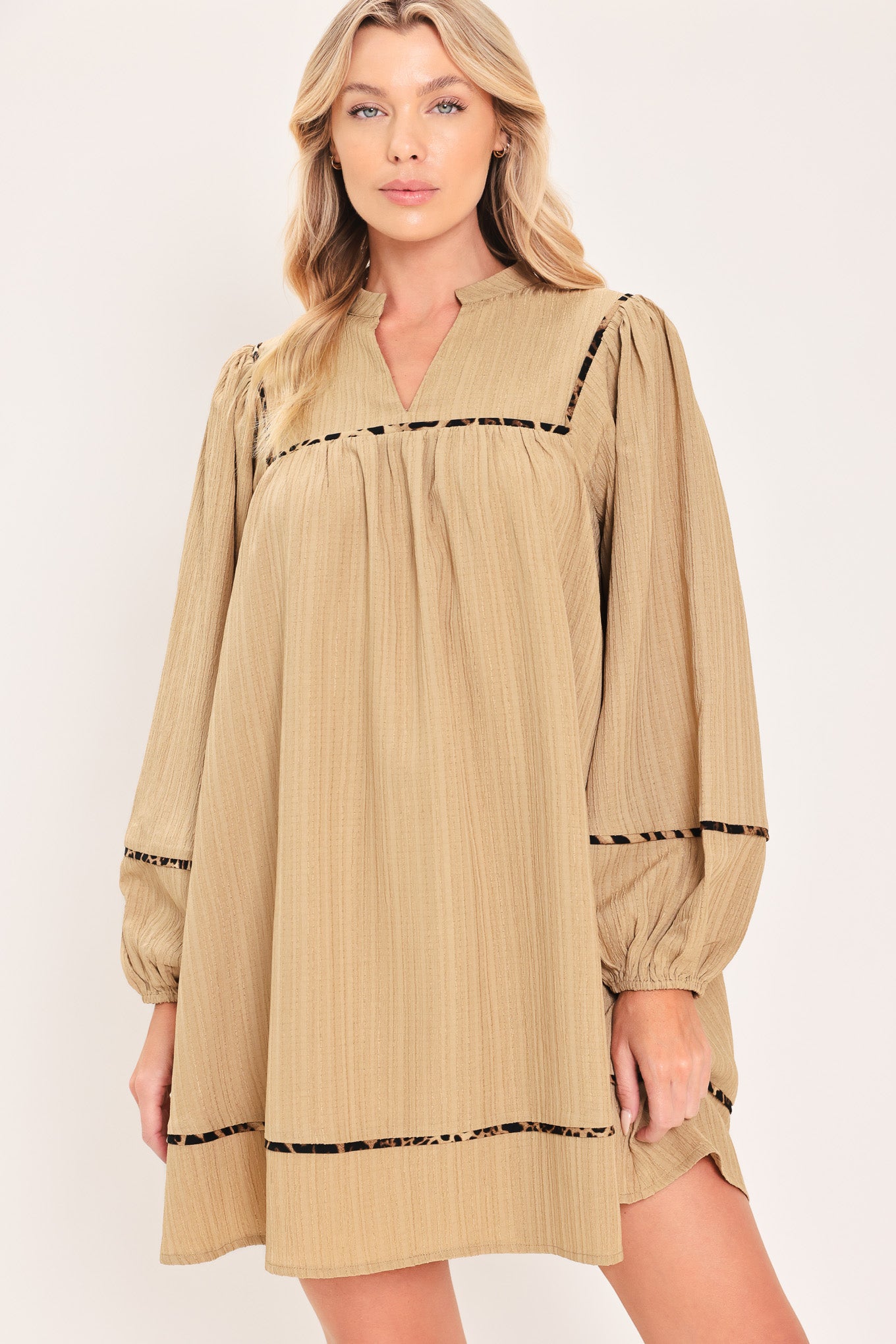 A woman wearing a beige long-sleeve mini dress with black leopard print patterned trim details | Flying Tomato