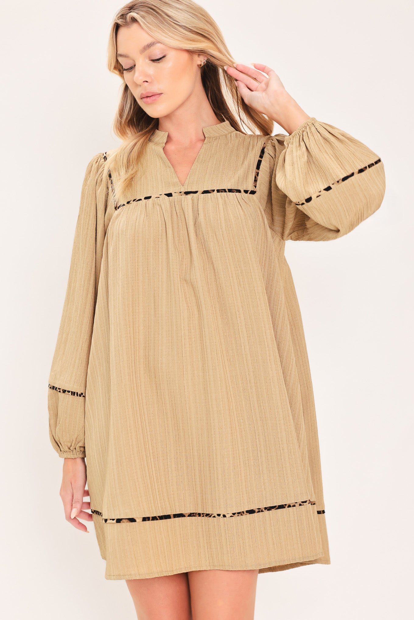 A woman wearing a beige long-sleeve mini dress with black leopard print patterned trim details | Flying Tomato