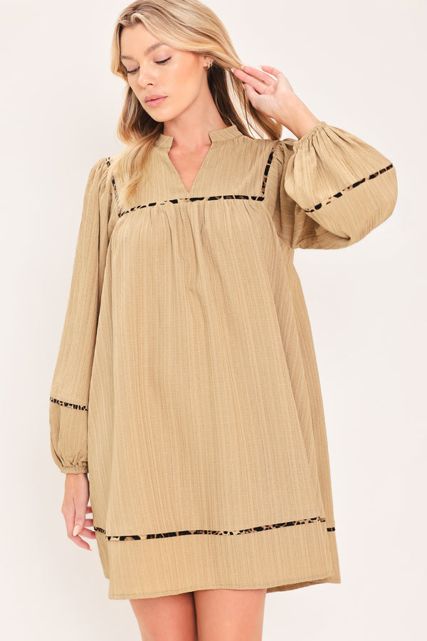 A woman wearing a beige long-sleeve mini dress with black leopard print patterned trim details | Flying Tomato
