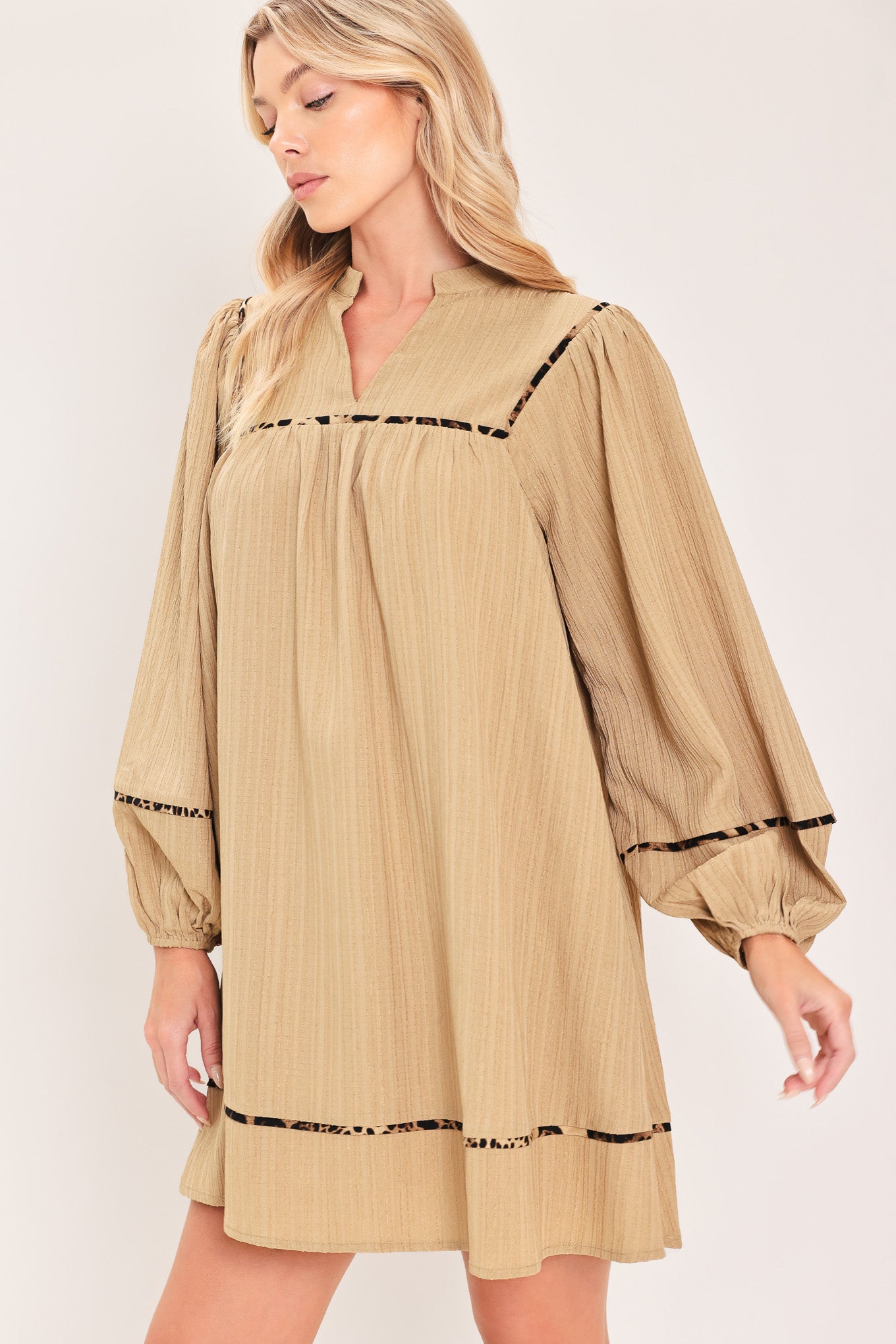 A woman wearing a beige long-sleeve mini dress with black leopard print patterned trim details | Flying Tomato