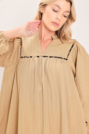 A woman wearing a beige long-sleeve mini dress with black leopard print patterned trim details | Flying Tomato