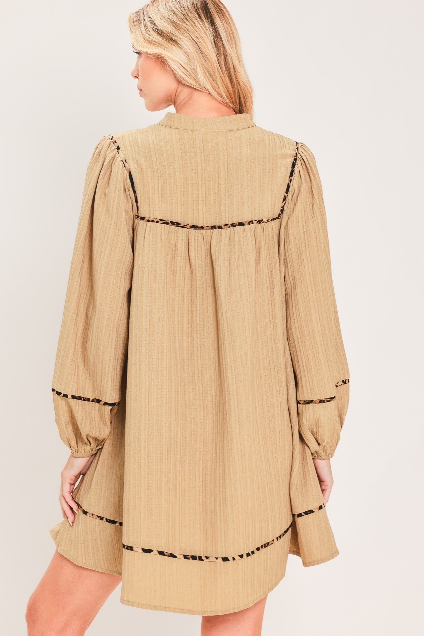 A woman wearing a beige long-sleeve mini dress with black leopard print patterned trim details | Flying Tomato