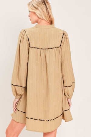A woman wearing a beige long-sleeve mini dress with black leopard print patterned trim details | Flying Tomato