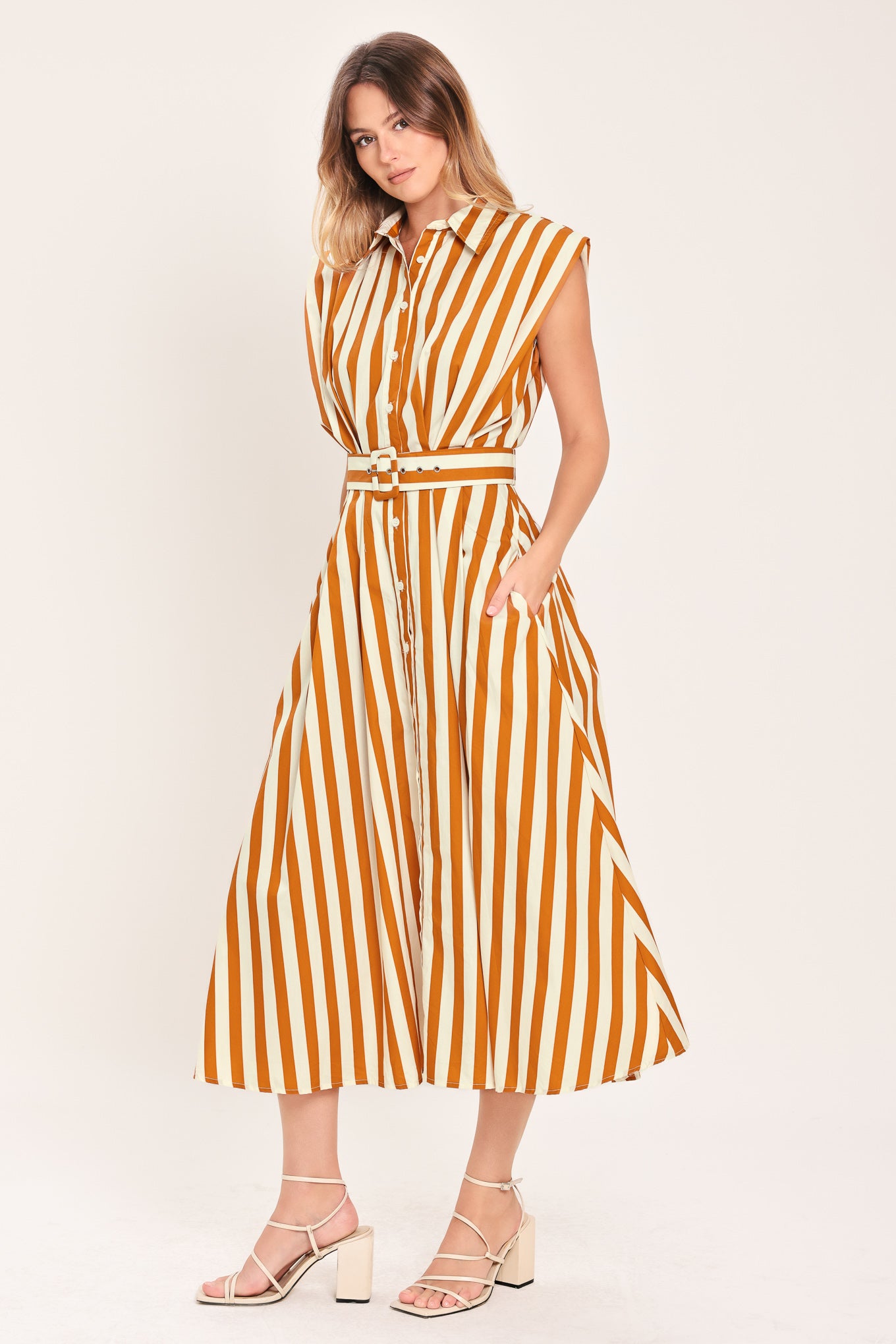 Woman wearing a sleeveless caramel and white striped dress with a belt | Flying Tomato