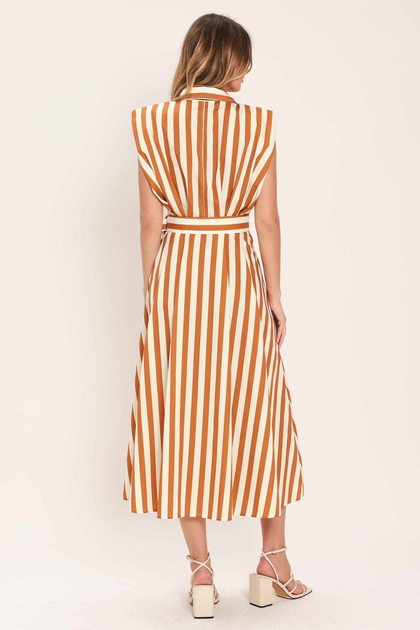 Woman wearing a sleeveless caramel and white striped dress with a belt | Flying Tomato