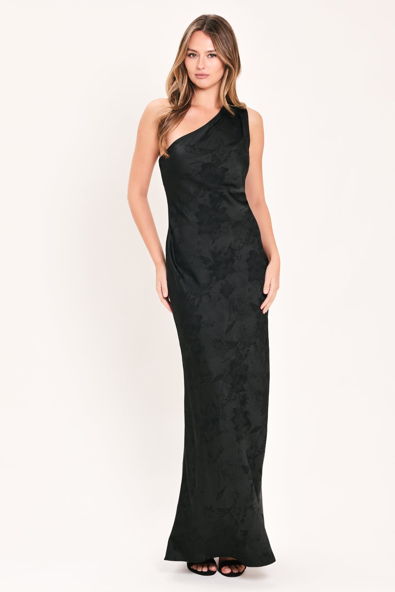 A woman modeling a sleeveless, one-shoulder black maxi dress with a textured jacquard pattern | Flying Tomato