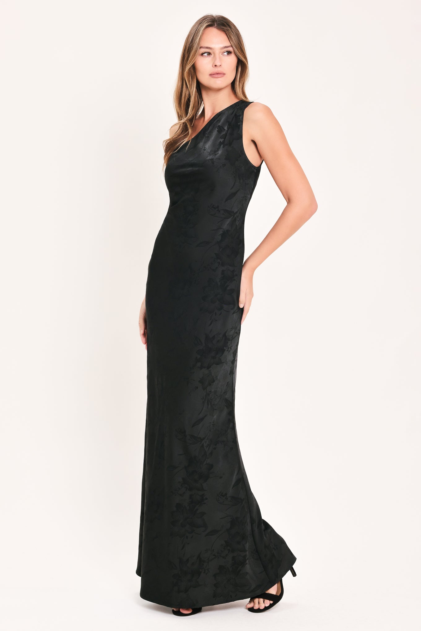 A woman modeling a sleeveless, one-shoulder black maxi dress with a textured jacquard pattern | Flying Tomato