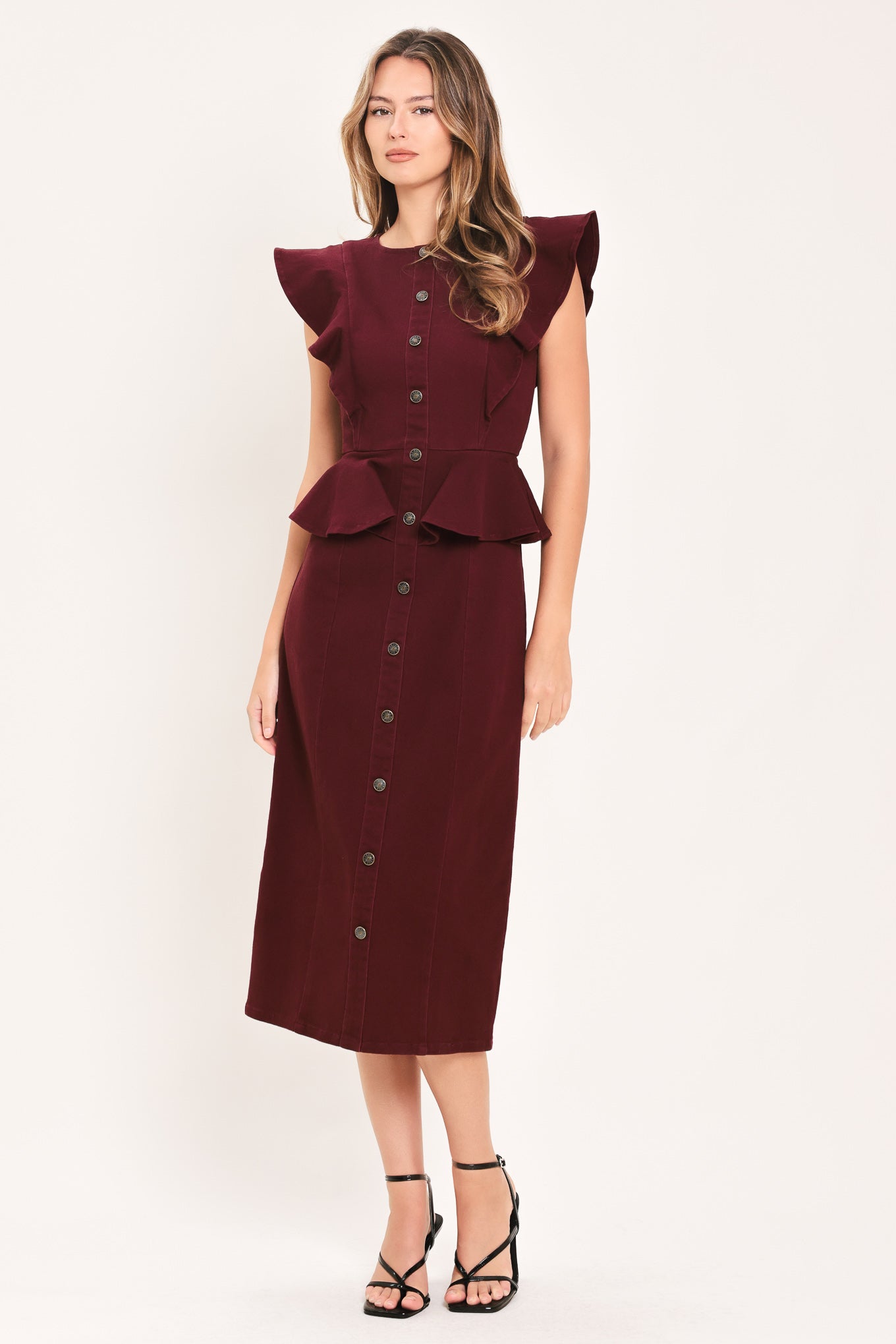 A woman modeling a sleeveless burgundy midi dress with ruffled cap sleeves, a peplum waist, and a front button placket | Flying Tomato