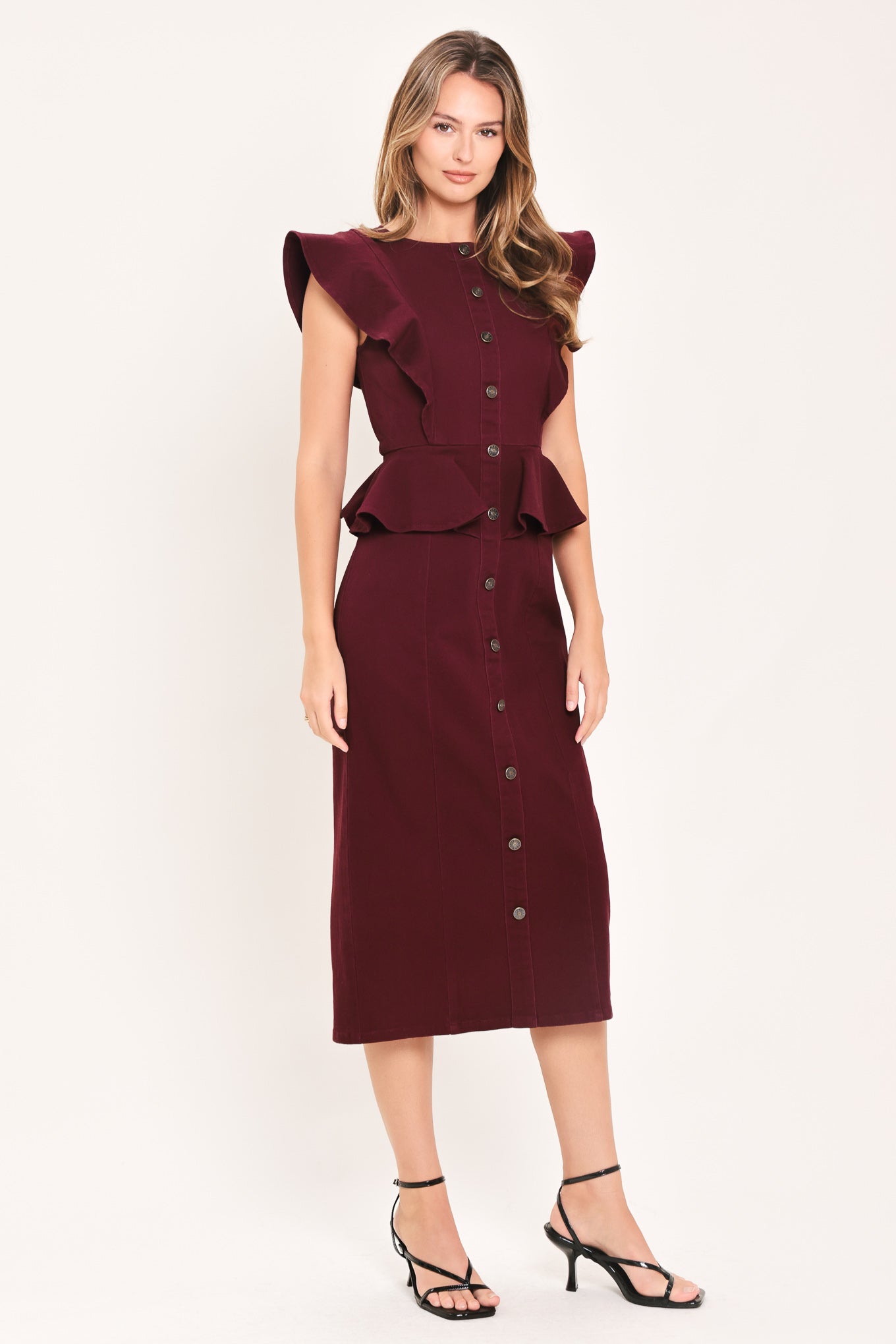 A woman modeling a sleeveless burgundy midi dress with ruffled cap sleeves, a peplum waist, and a front button placket | Flying Tomato