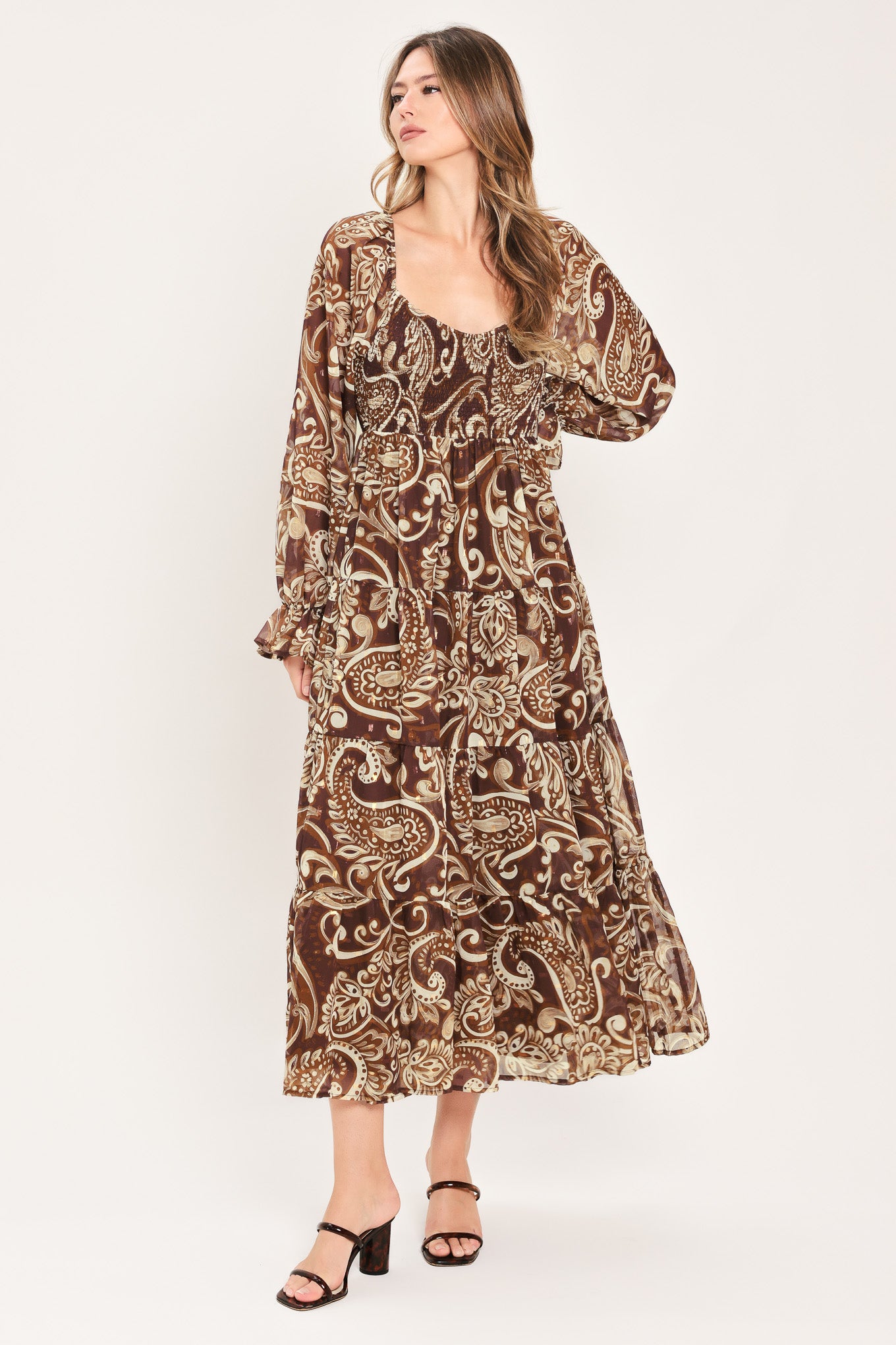 A woman wearing a long-sleeved midi dress with a brown and beige paisley pattern | Flying Tomato