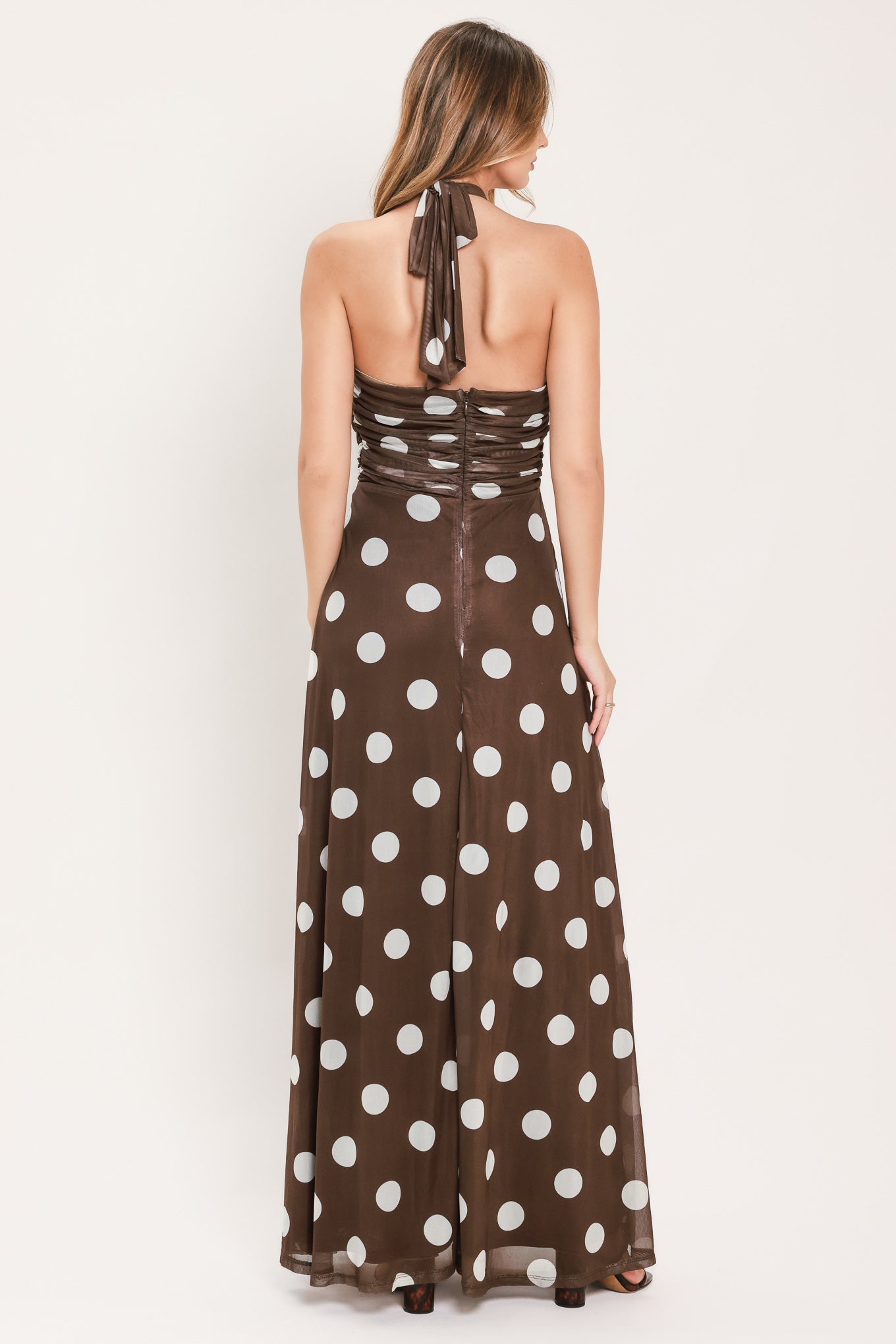 A woman modeling a brown halter-neck maxi dress with a white polka dot pattern | Flying Tomato