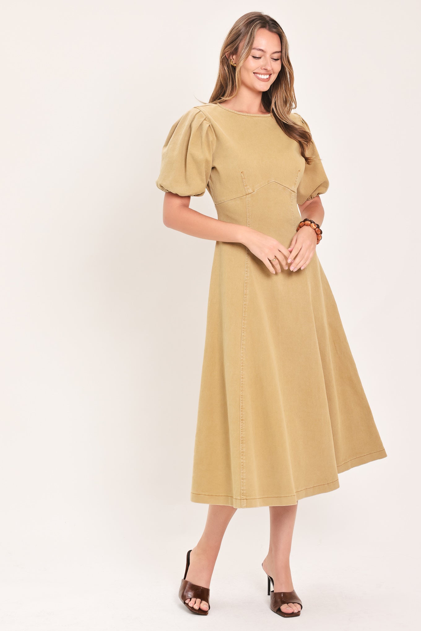 A woman modeling a tan midi dress with puff sleeves, a round neckline, and a flared skirt | Flying Tomato