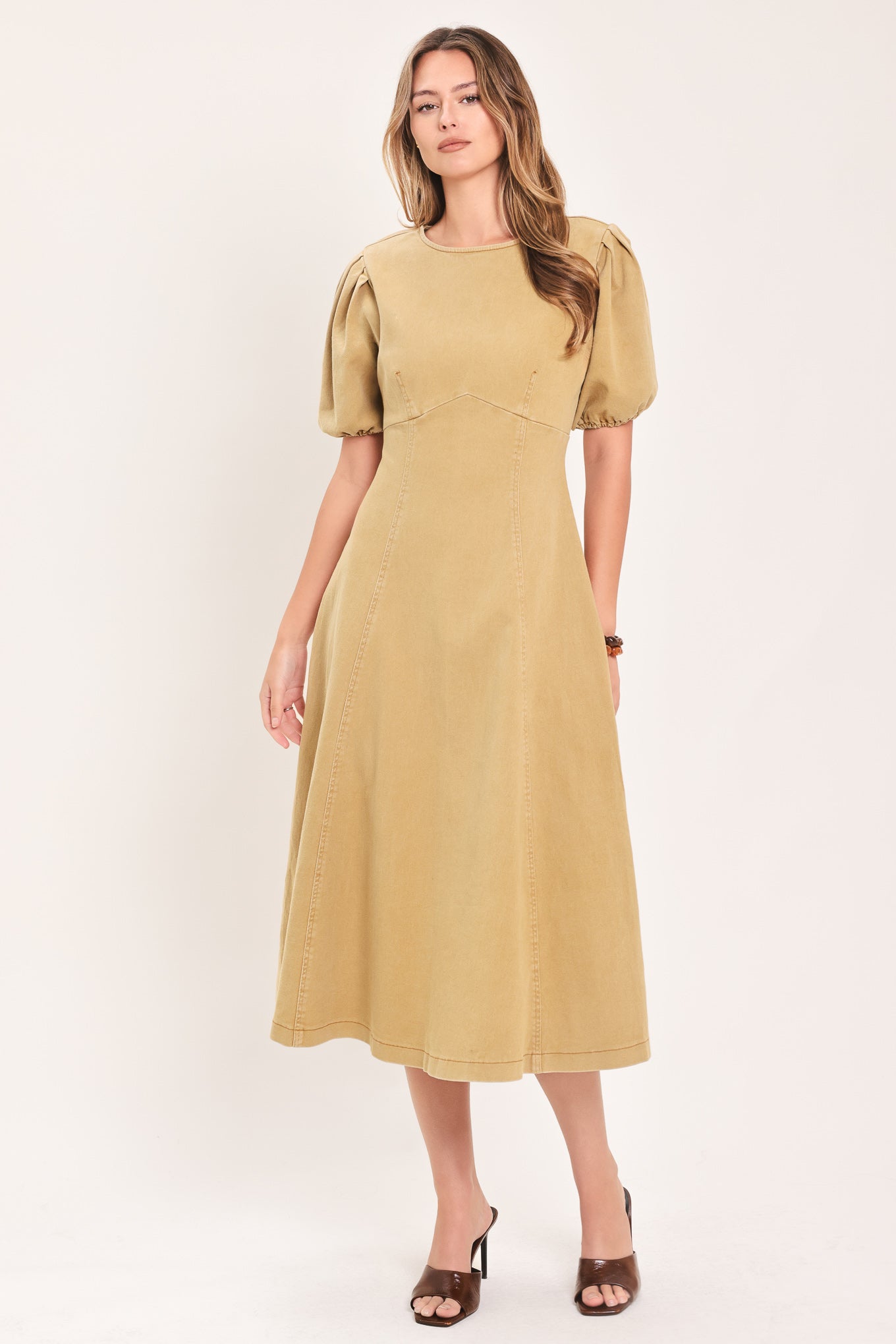 A woman modeling a tan midi dress with puff sleeves, a round neckline, and a flared skirt | Flying Tomato