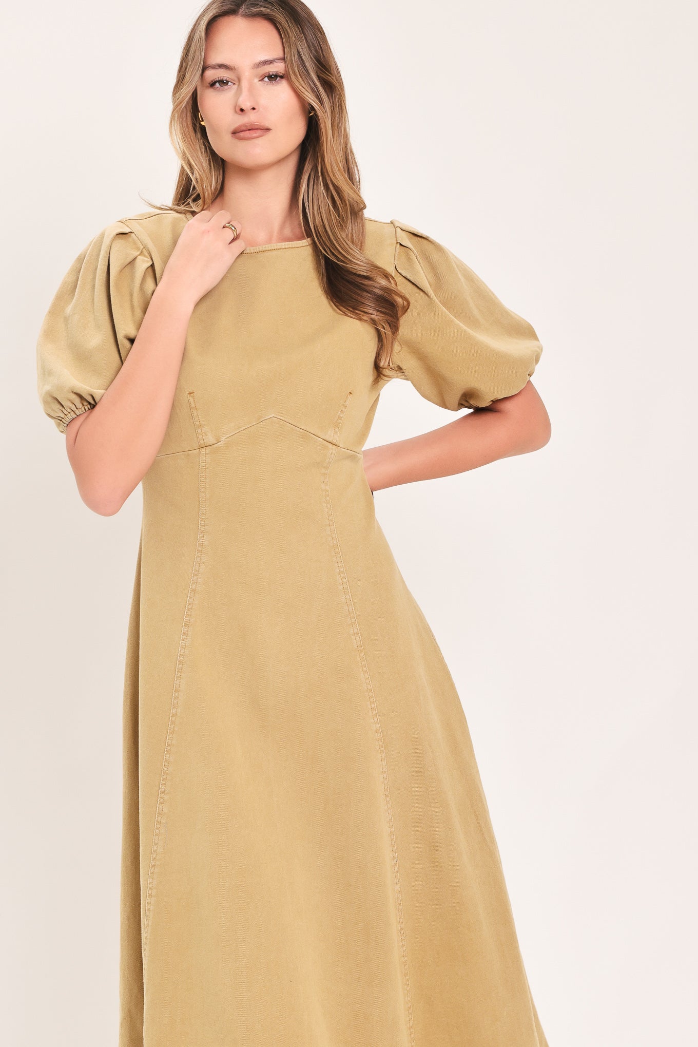 A woman modeling a tan midi dress with puff sleeves, a round neckline, and a flared skirt | Flying Tomato
