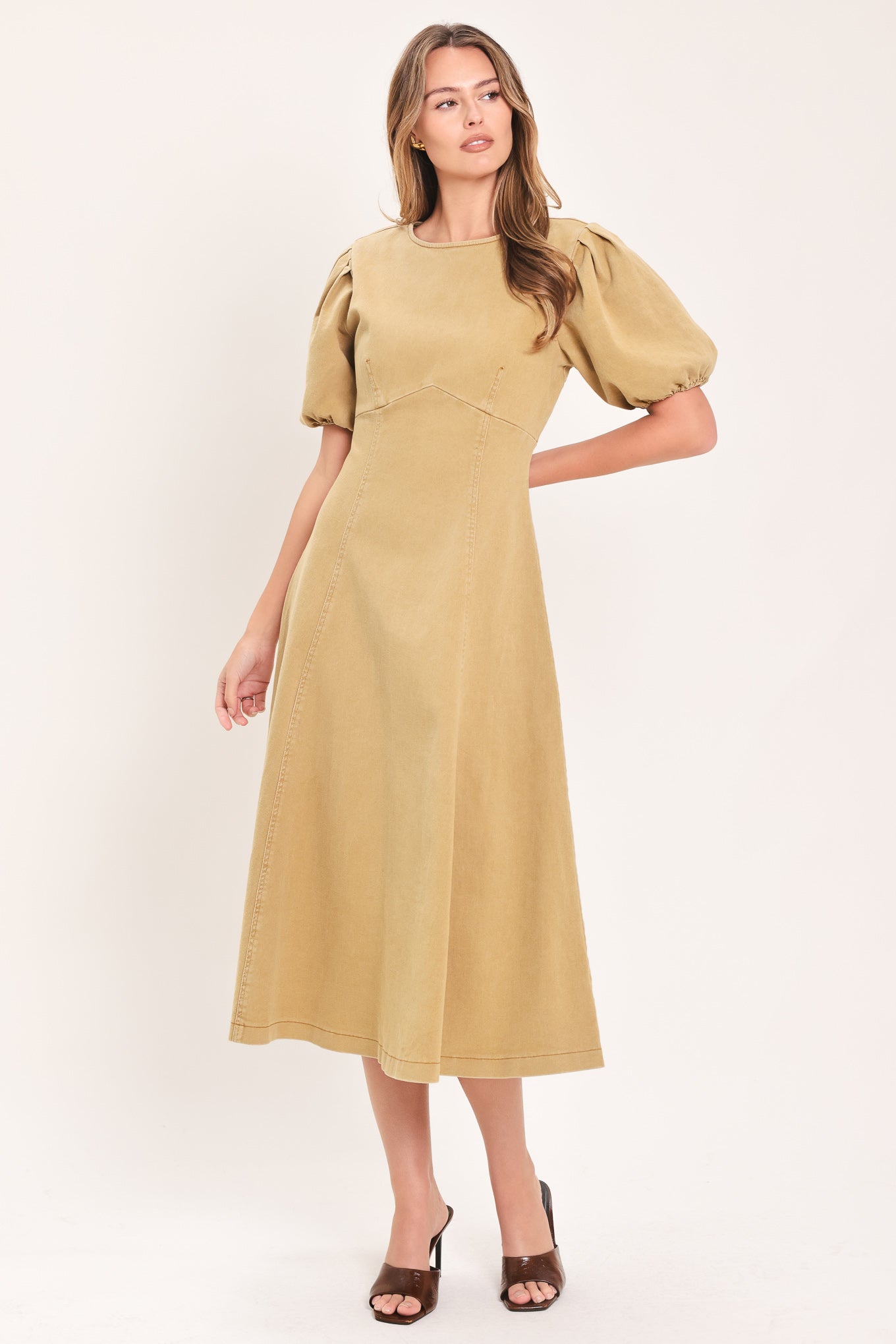 A woman modeling a tan midi dress with puff sleeves, a round neckline, and a flared skirt | Flying Tomato
