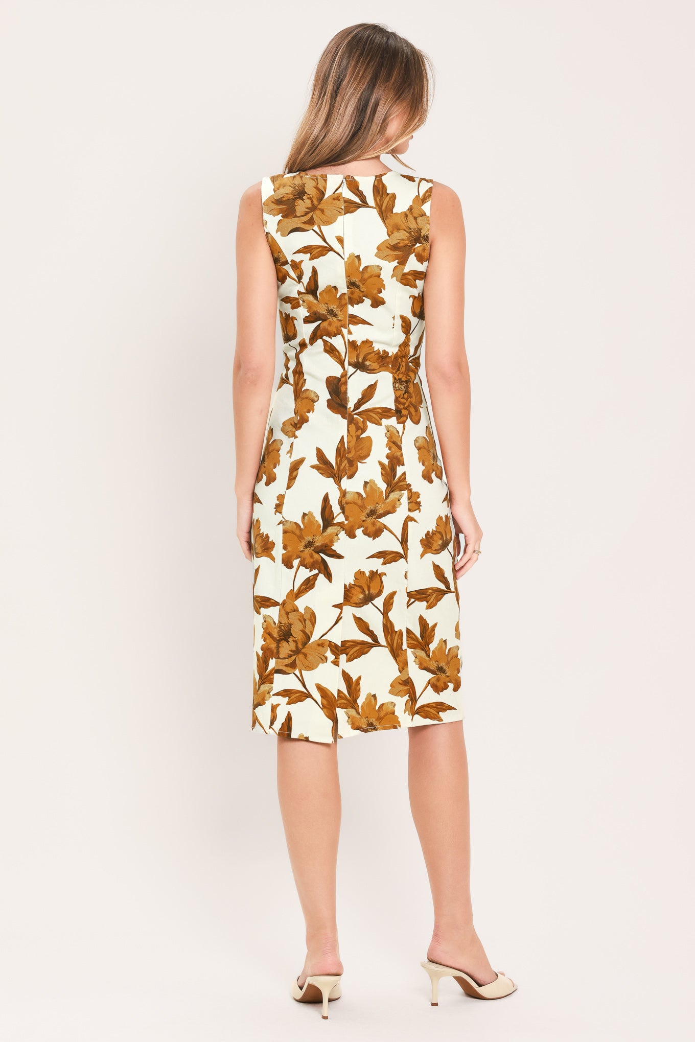 A woman modeling a sleeveless midi dress with a warm cream background and a large brown floral print | Flying Tomato