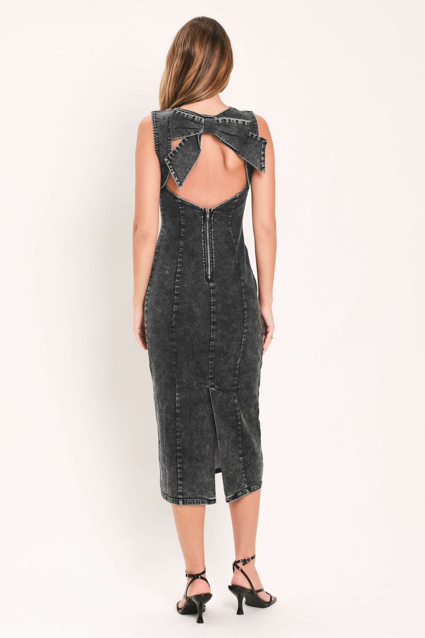 A woman modeling a sleeveless, bodycon midi dress in a washed charcoal gray denim fabric with a large bow detail at the open back | Flying Tomato