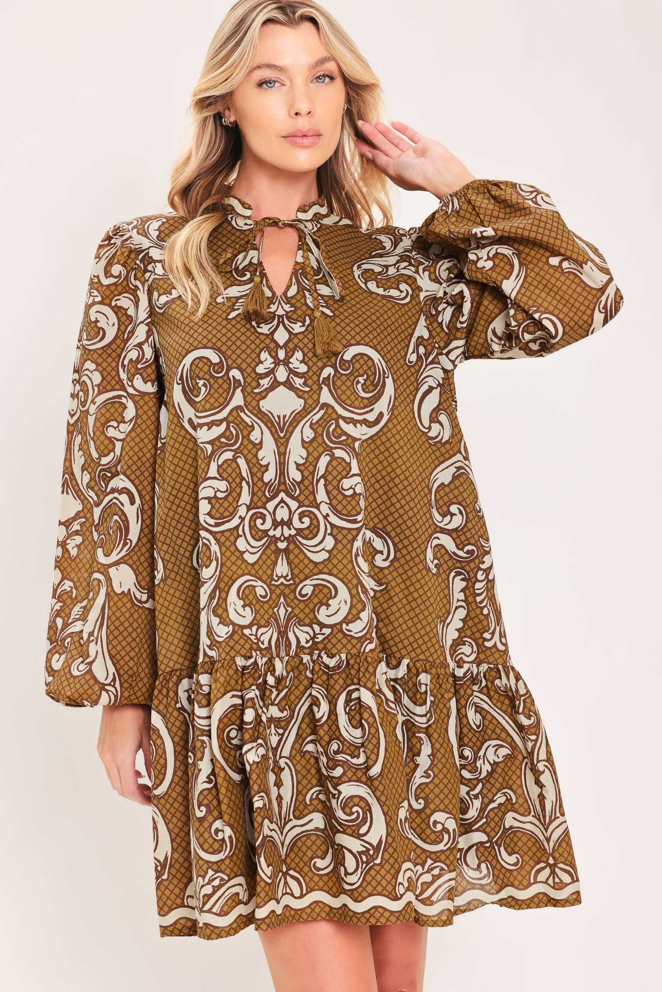 A woman wearing a long-sleeve mini dress with a brown and beige baroque scroll pattern, featuring a keyhole tie neckline and balloon sleeves | Flying Tomato