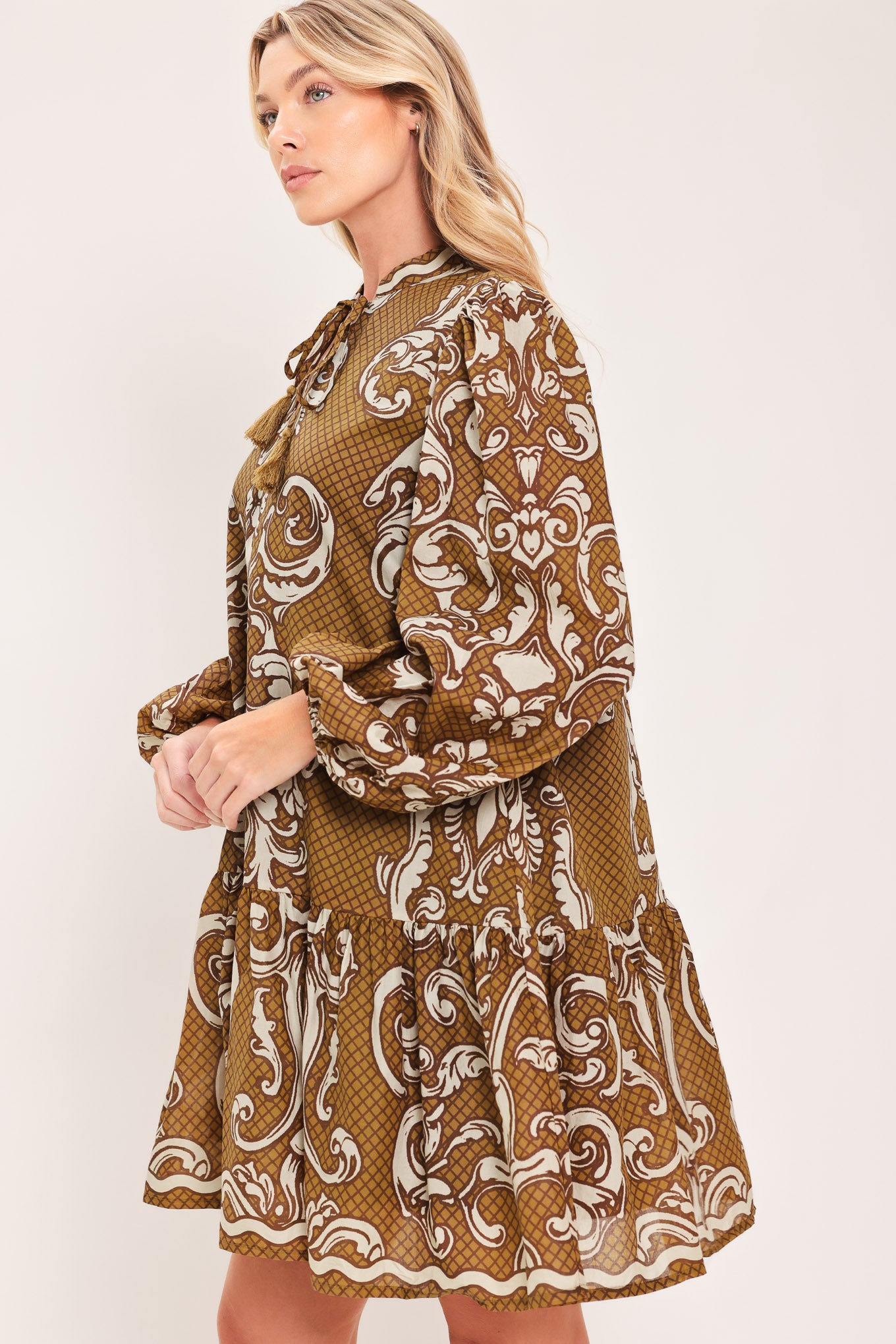 A woman wearing a long-sleeve mini dress with a brown and beige baroque scroll pattern, featuring a keyhole tie neckline and balloon sleeves | Flying Tomato