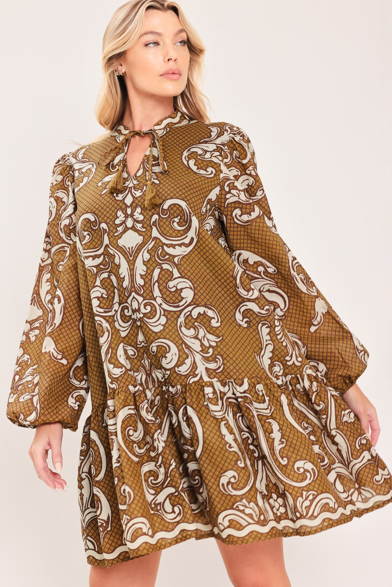 A woman wearing a long-sleeve mini dress with a brown and beige baroque scroll pattern, featuring a keyhole tie neckline and balloon sleeves | Flying Tomato