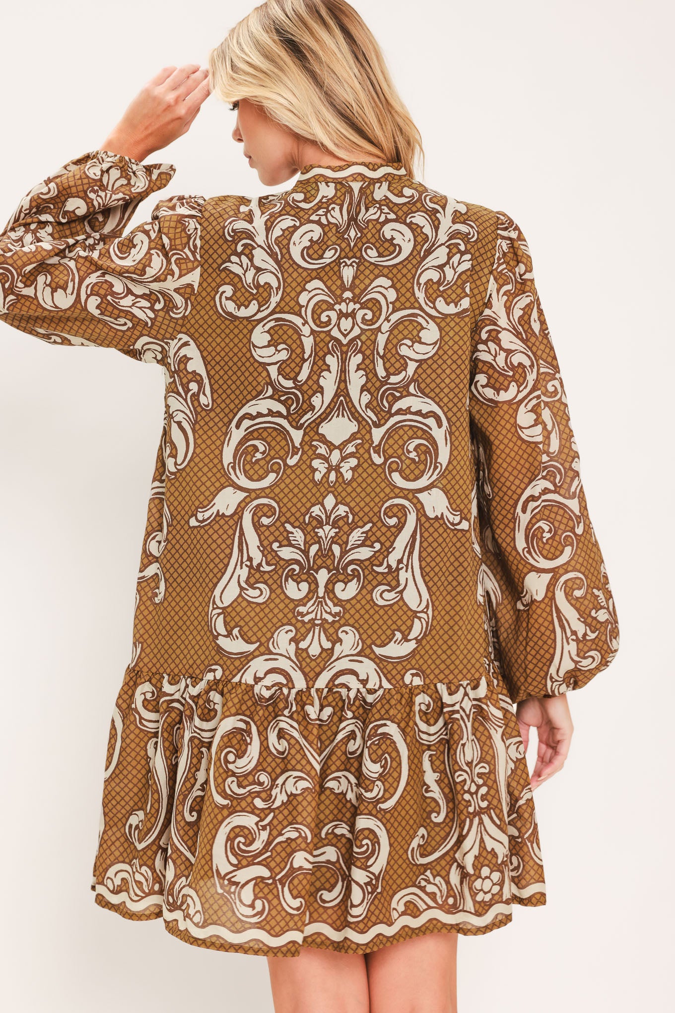 A woman wearing a long-sleeve mini dress with a brown and beige baroque scroll pattern, featuring a keyhole tie neckline and balloon sleeves | Flying Tomato