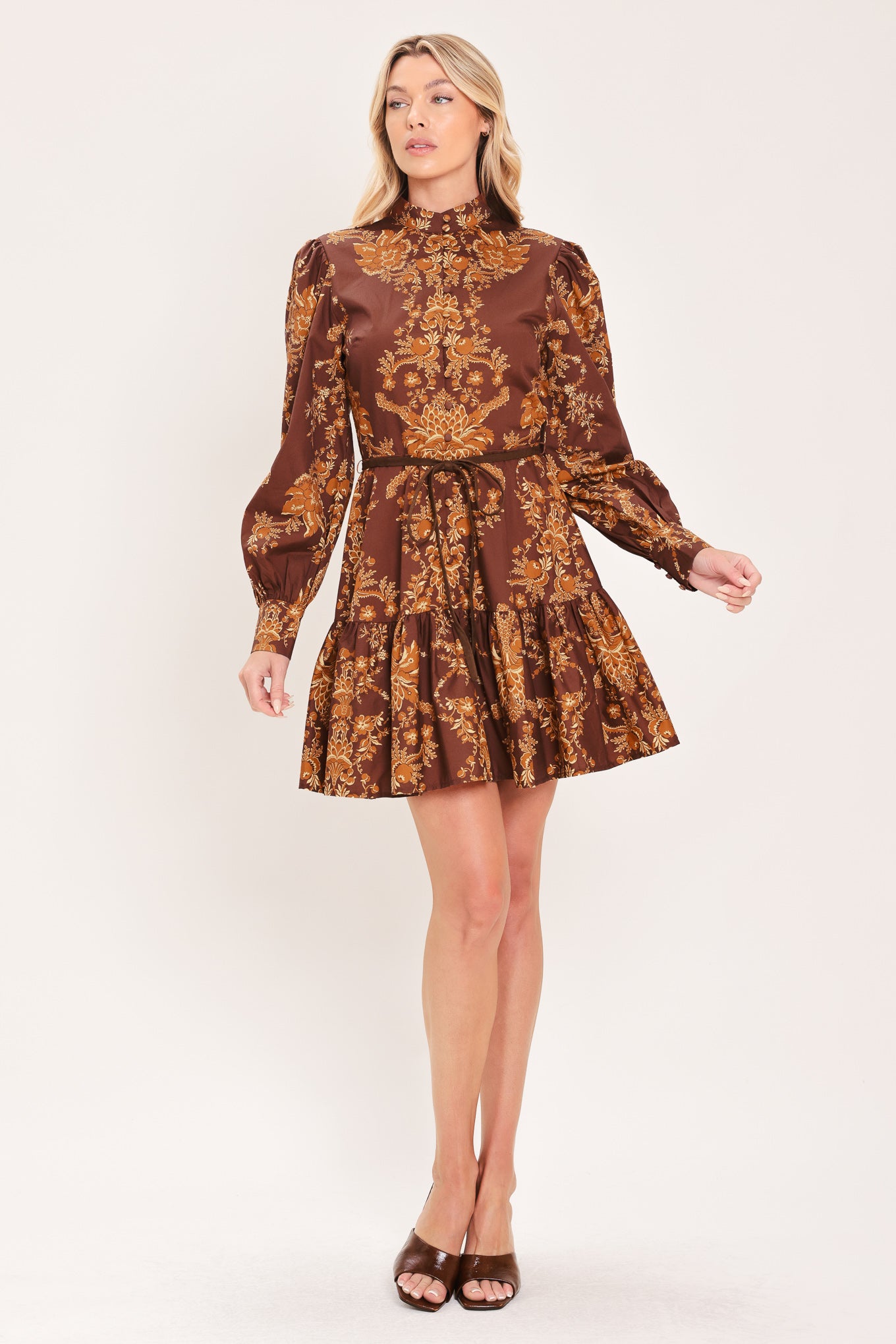 A woman modeling a brown and gold damask-patterned long-sleeve mini dress with a high mock neck and a matching waist tie | Flying Tomato